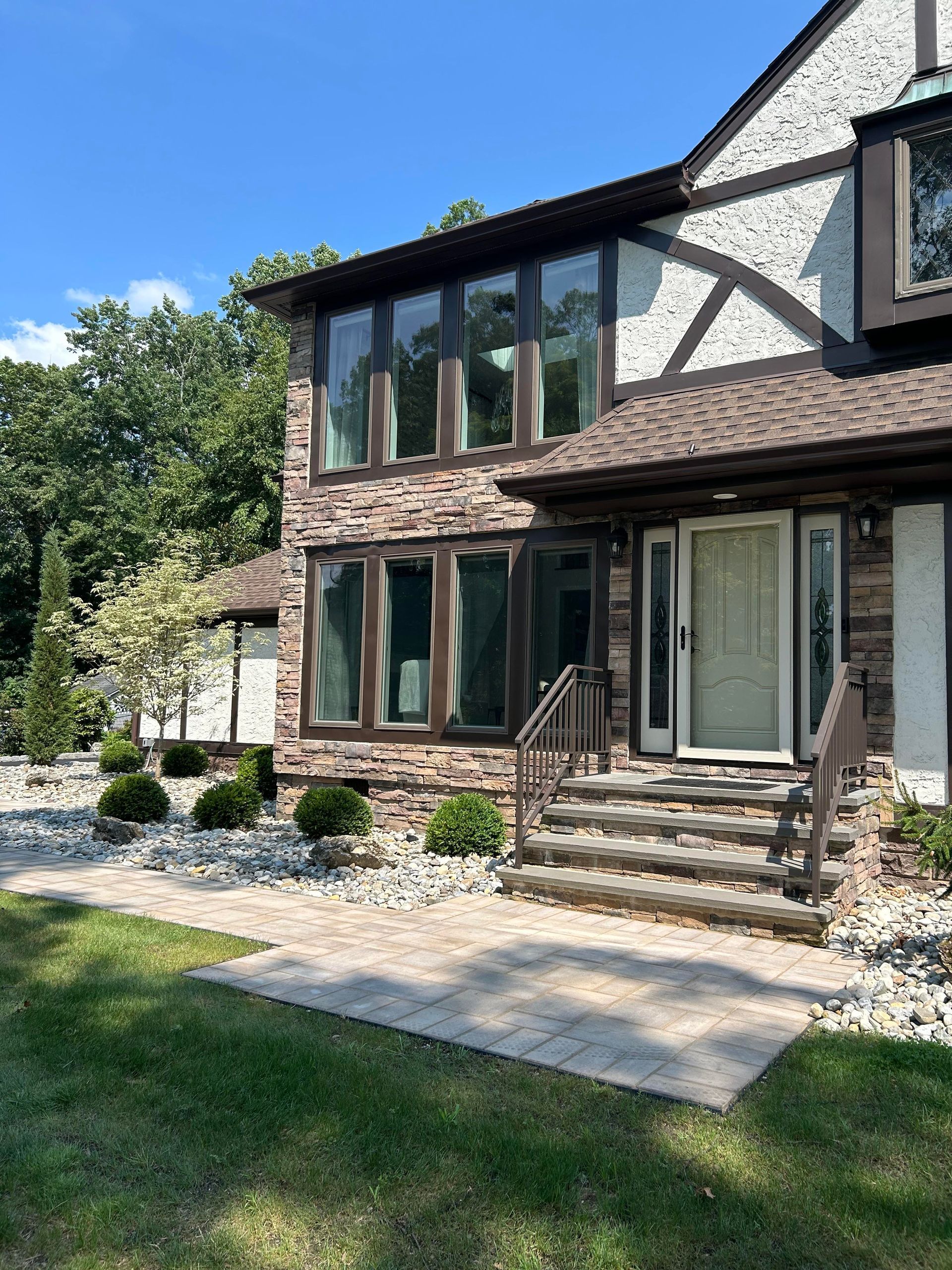 Two-story brick house with large windows, front steps, and a stone walkway in a sunny yard