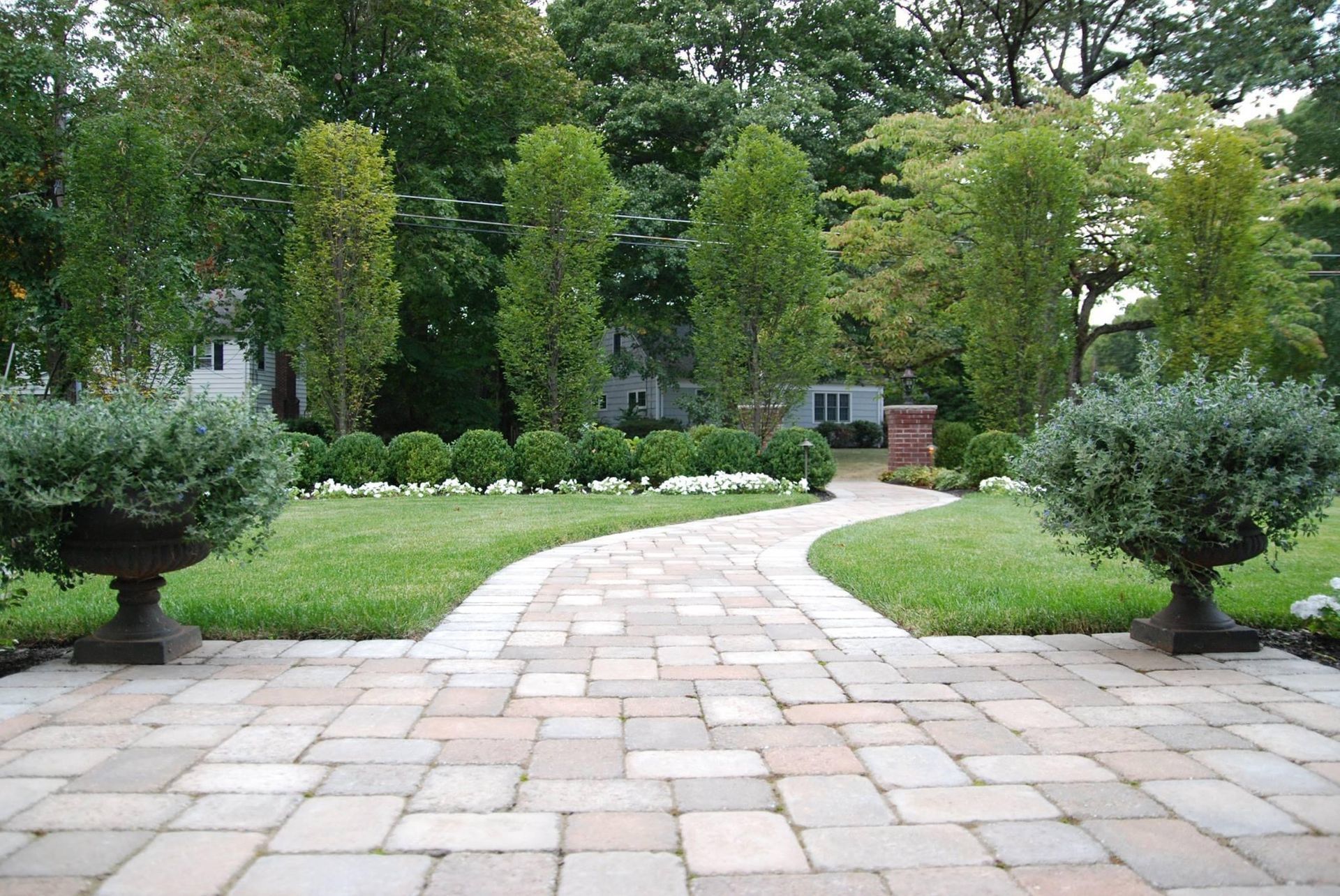 Stone path winding through a lush green garden with trimmed shrubs and tall trees