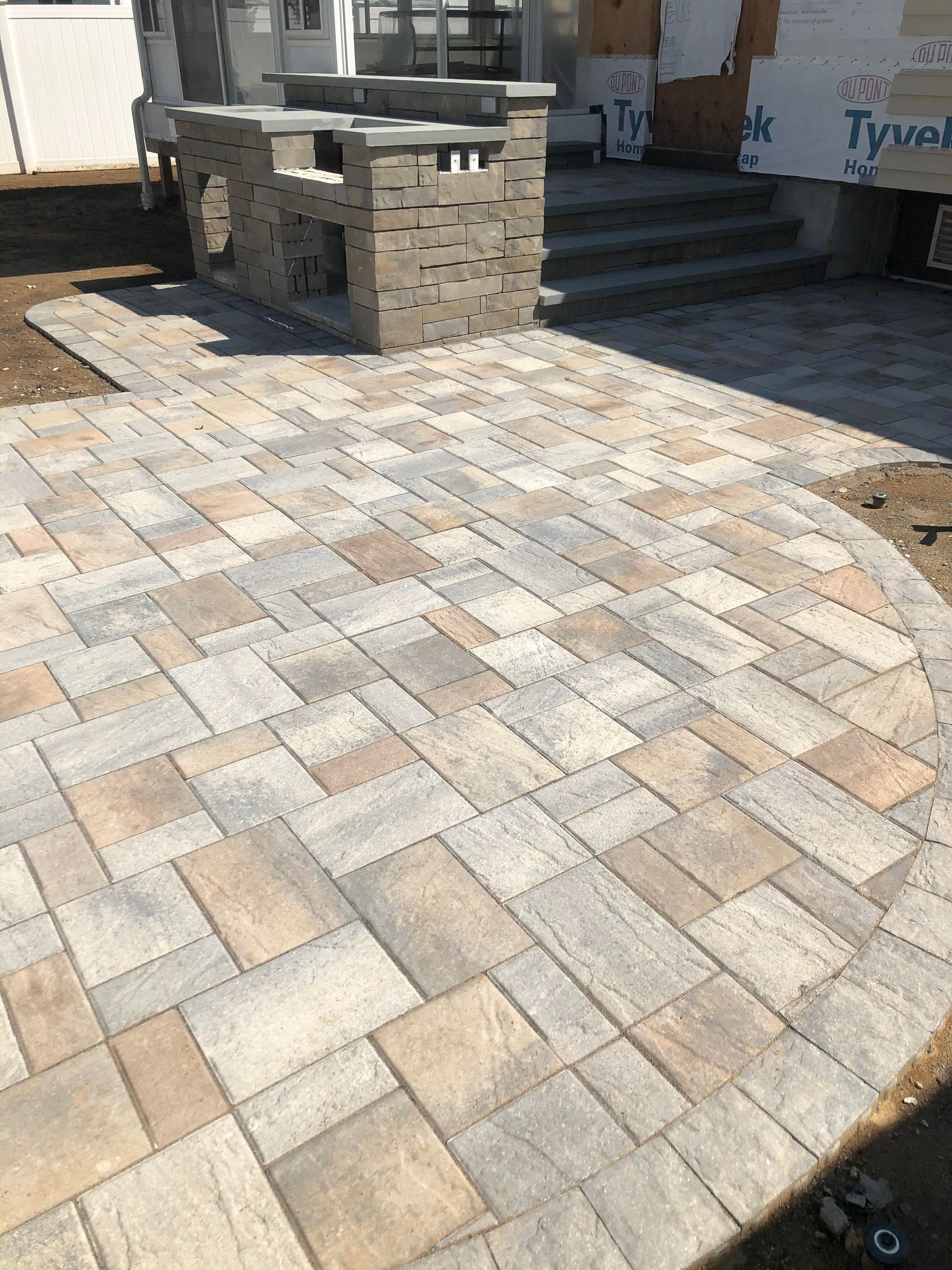 Stone paver patio with a built-in outdoor grill near a house entrance