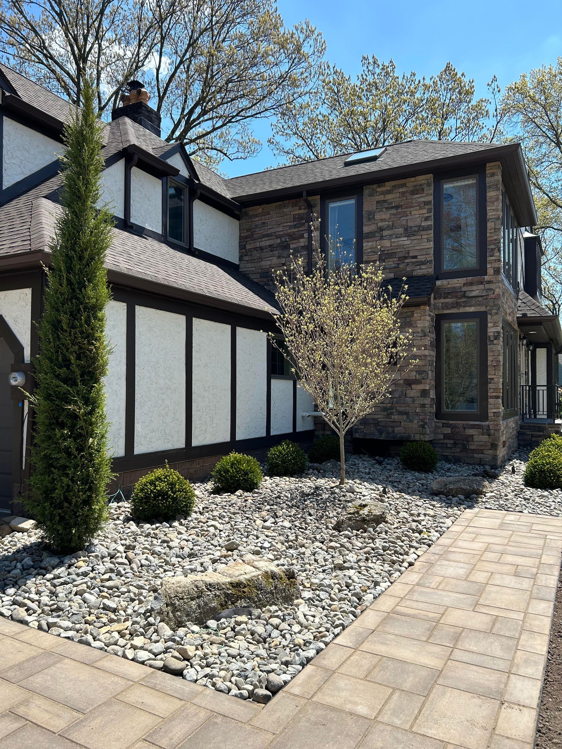 Modern two-story house with white-and-black exterior, stone facade, and landscaped front yard with gravel and pavers