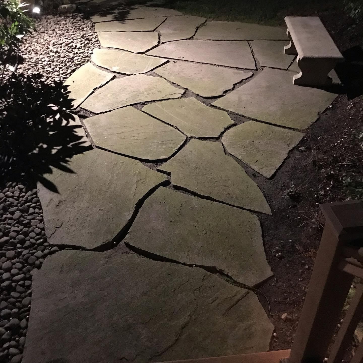 Stone garden path lit at night, with a bench on the right and landscaping along the edges