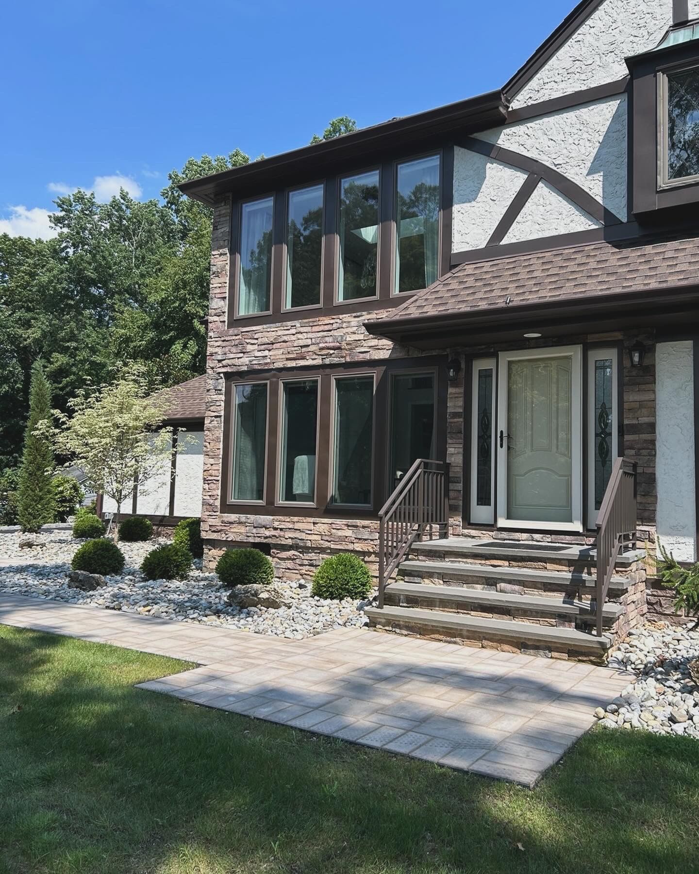 Suburban house exterior with stone façade, front porch, steps, and landscaped yard on a sunny day