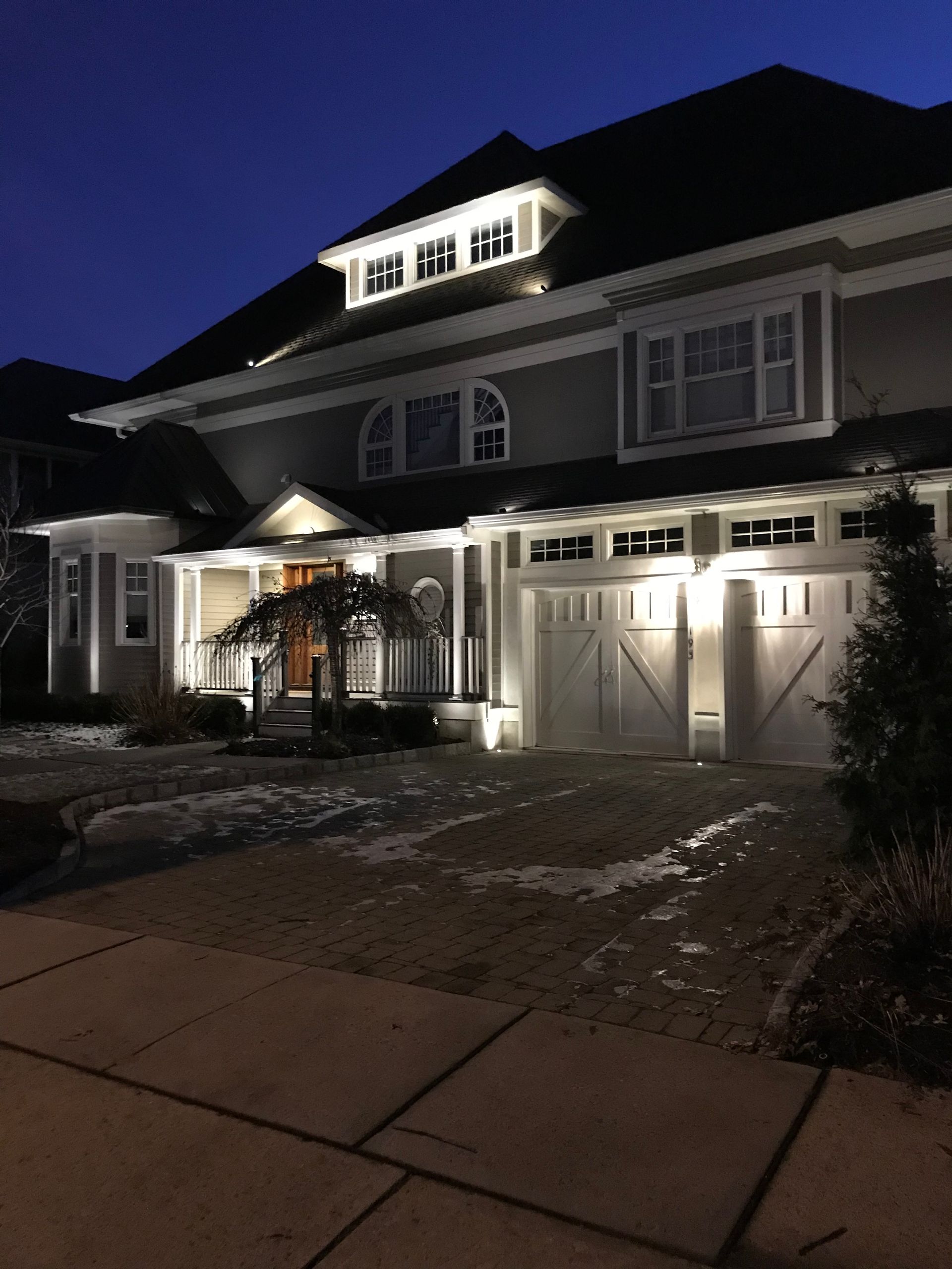 A two-story suburban house lit at night, with snow on the ground and a dark blue sky.