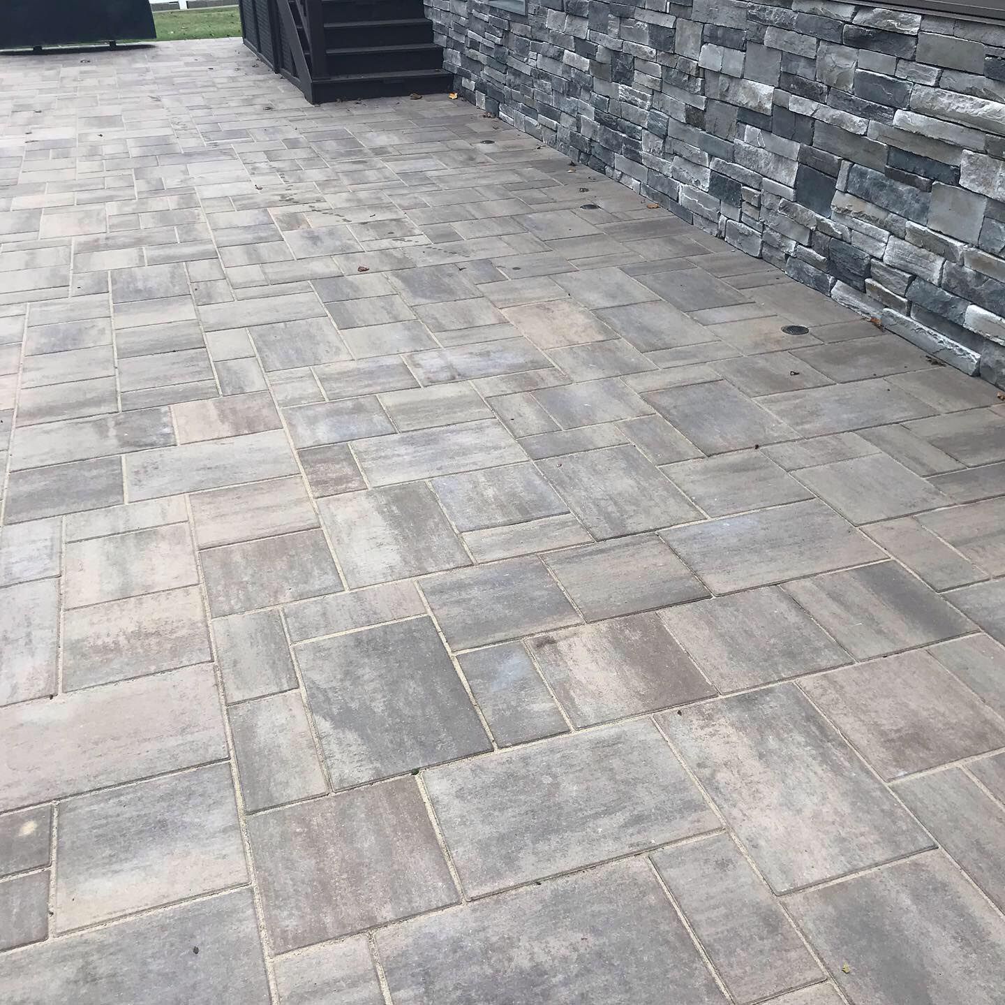 Gray stone patio with large pavers beside a dark stone wall and steps