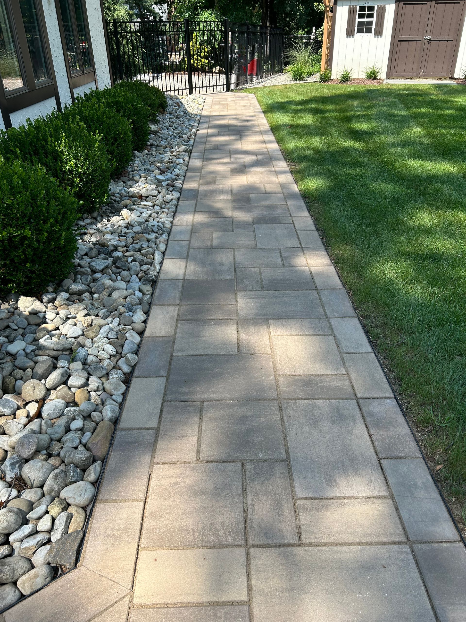 Stone paver walkway beside a lawn and white rock border leading to a house entrance