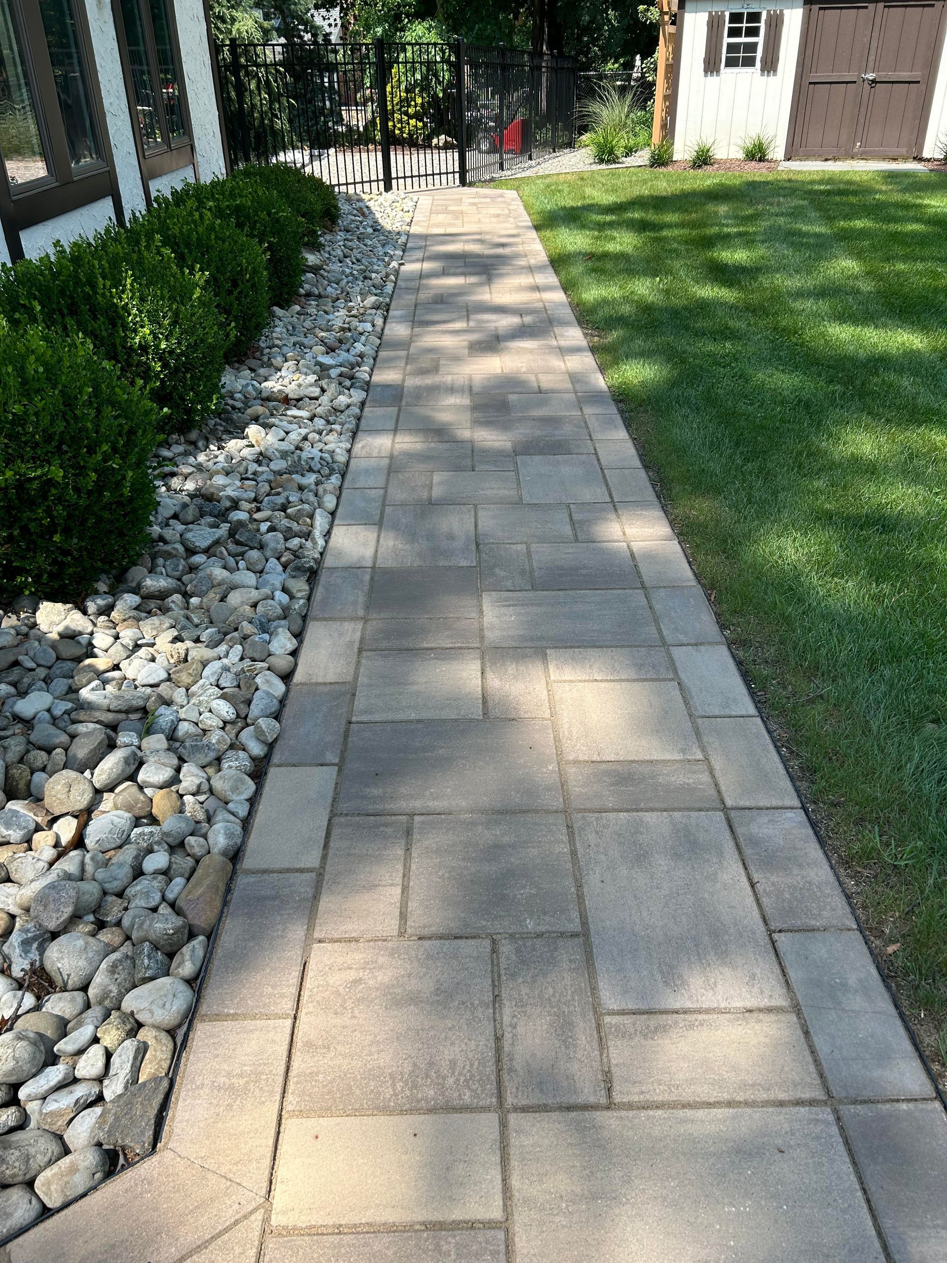 Stone walkway beside rocks and grass leading to a house entrance in a sunny yard