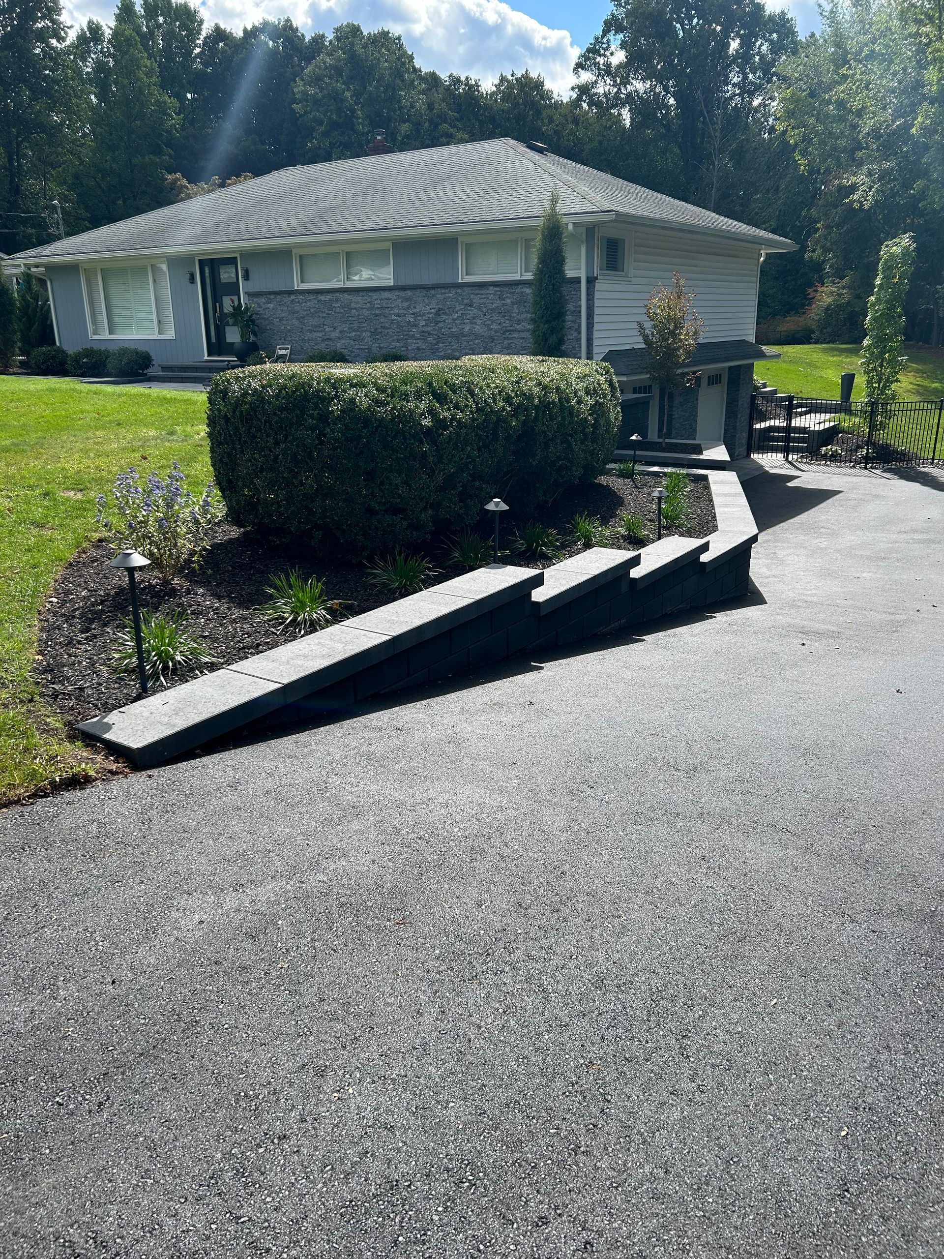 Residential driveway with a tipped-over metal ramp beside a trimmed hedge and house exterior