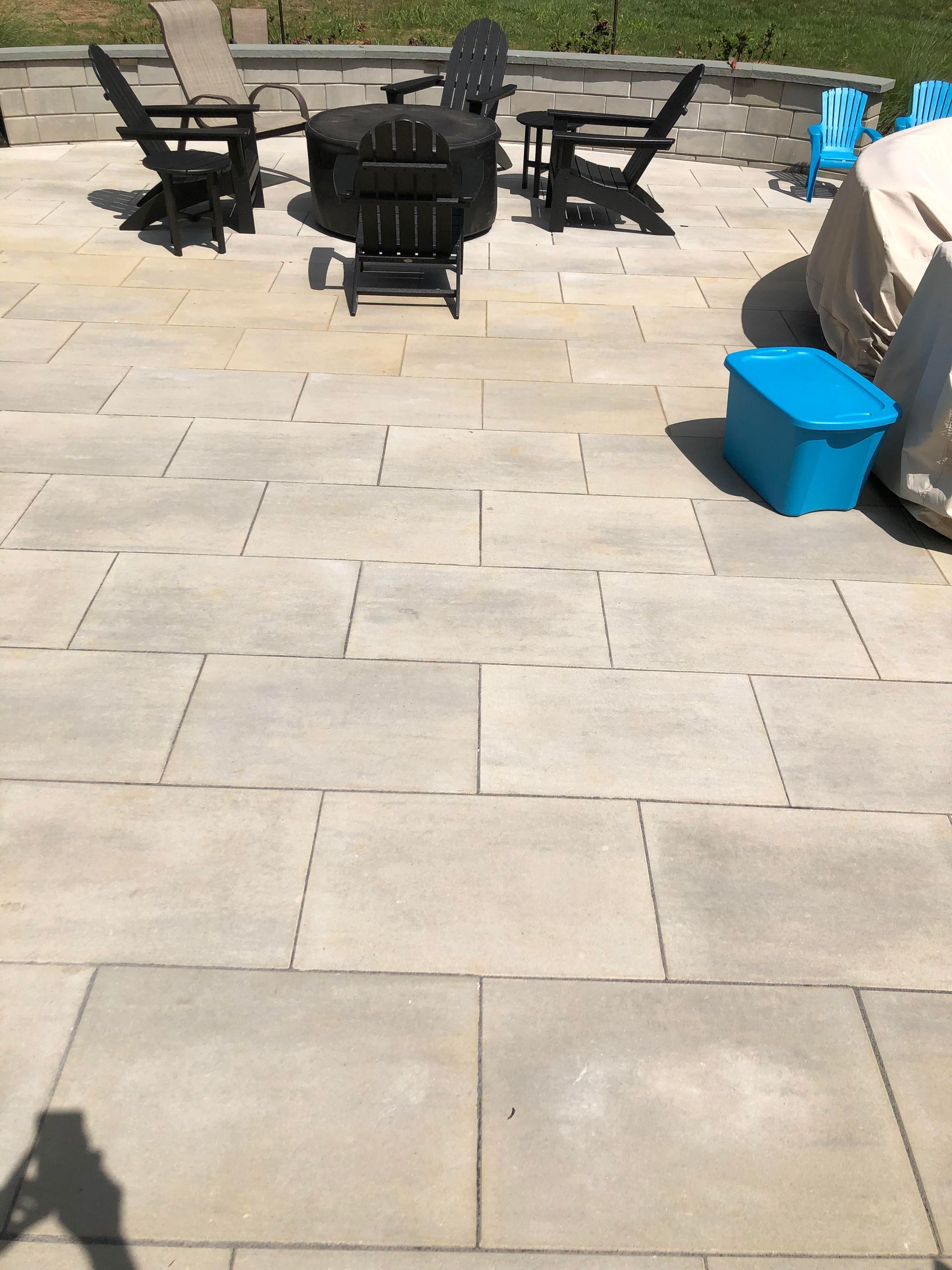 Patio with black outdoor chairs around a table on a stone terrace, with a blue storage bin on the right.