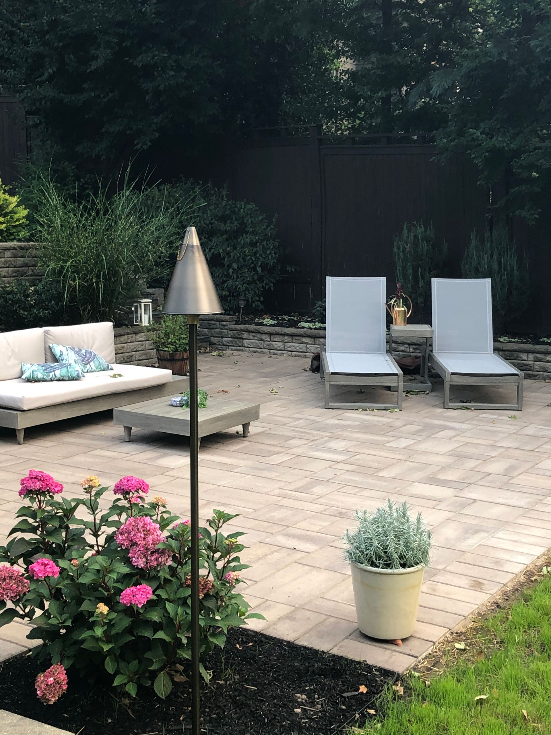 Patio with two lounge chairs, outdoor lamp, and potted flowers in a landscaped backyard