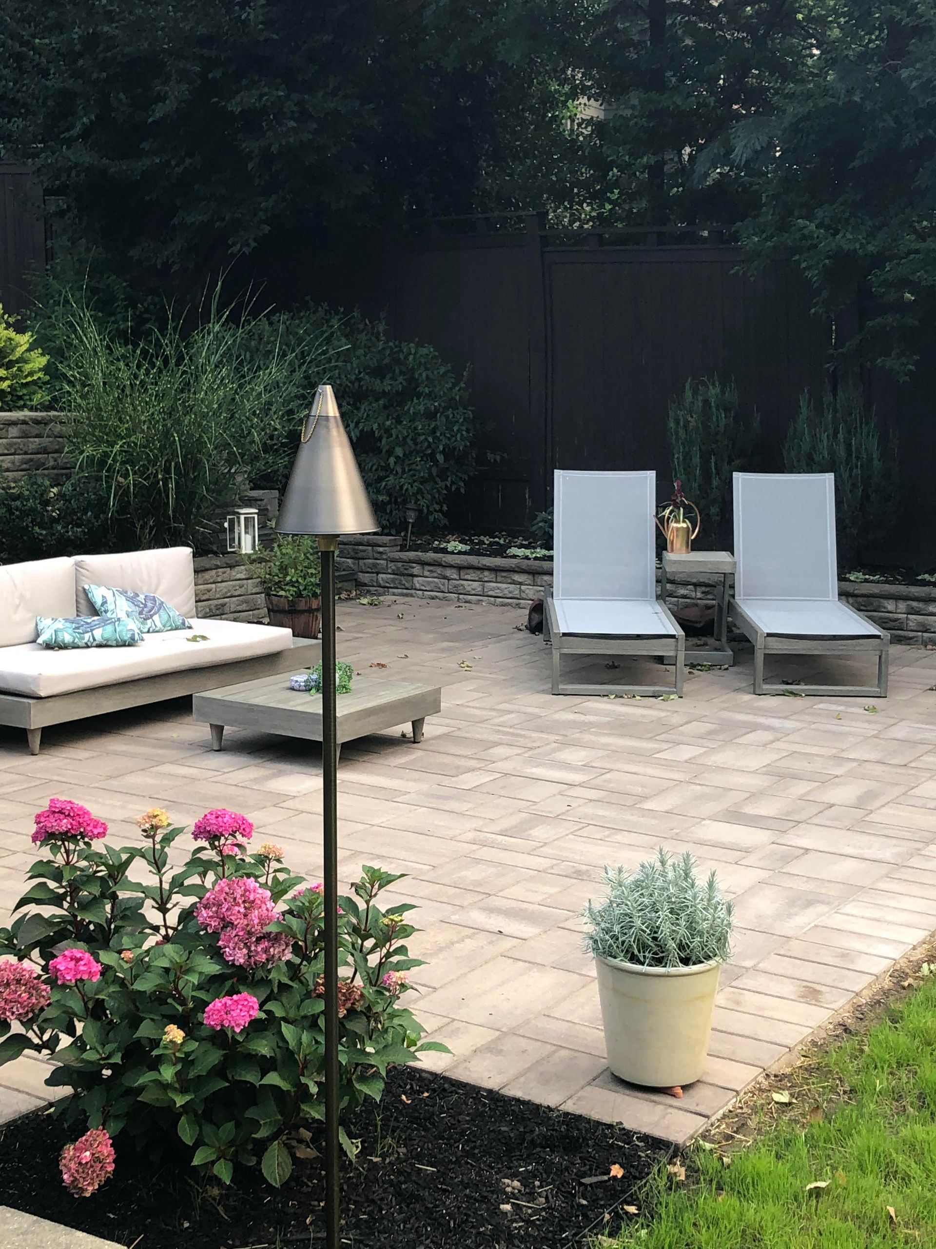 Backyard patio with lounge chairs, sofa, and potted flowers beside a gravel and stone seating area