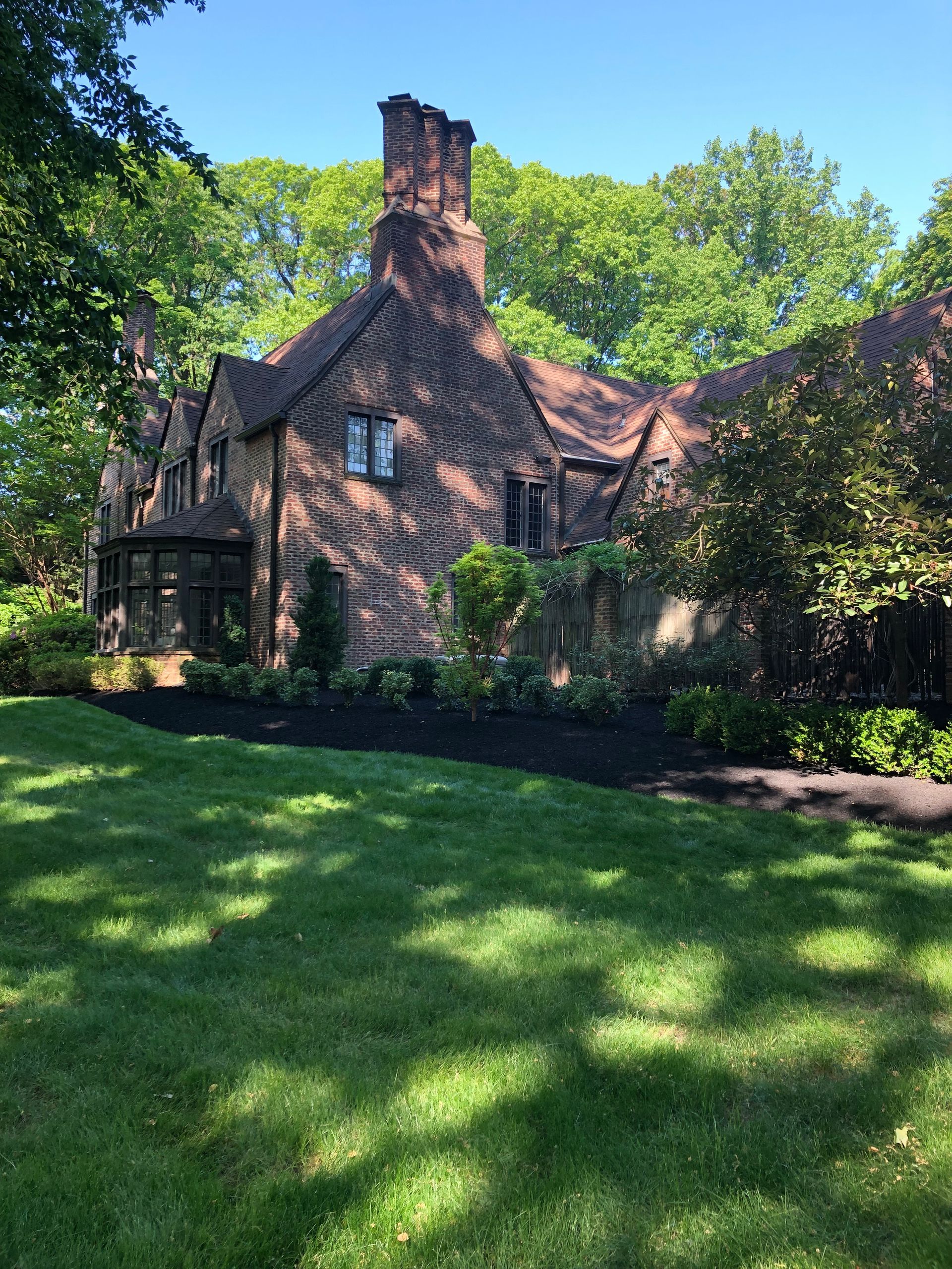 Stone cottage with a tall chimney, framed by trees and a sunlit green lawn.
