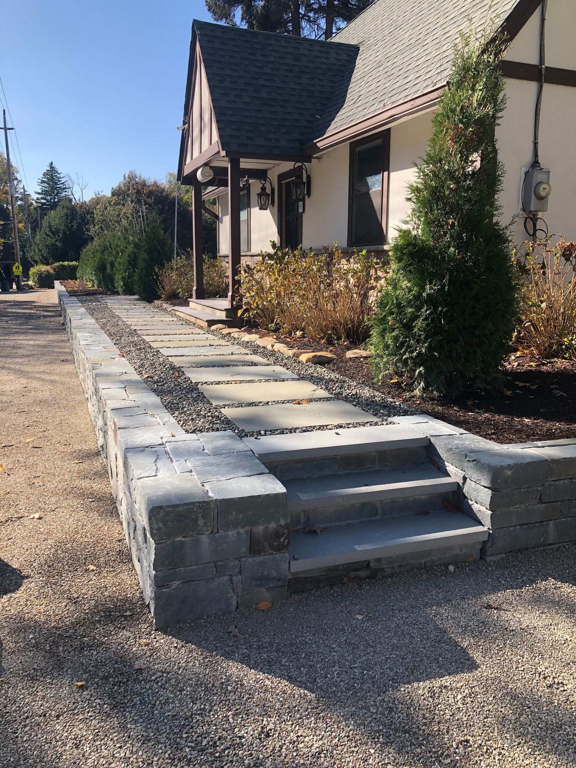 Stone walkway with steps leading to a house entrance, lined with gravel and shrubs.