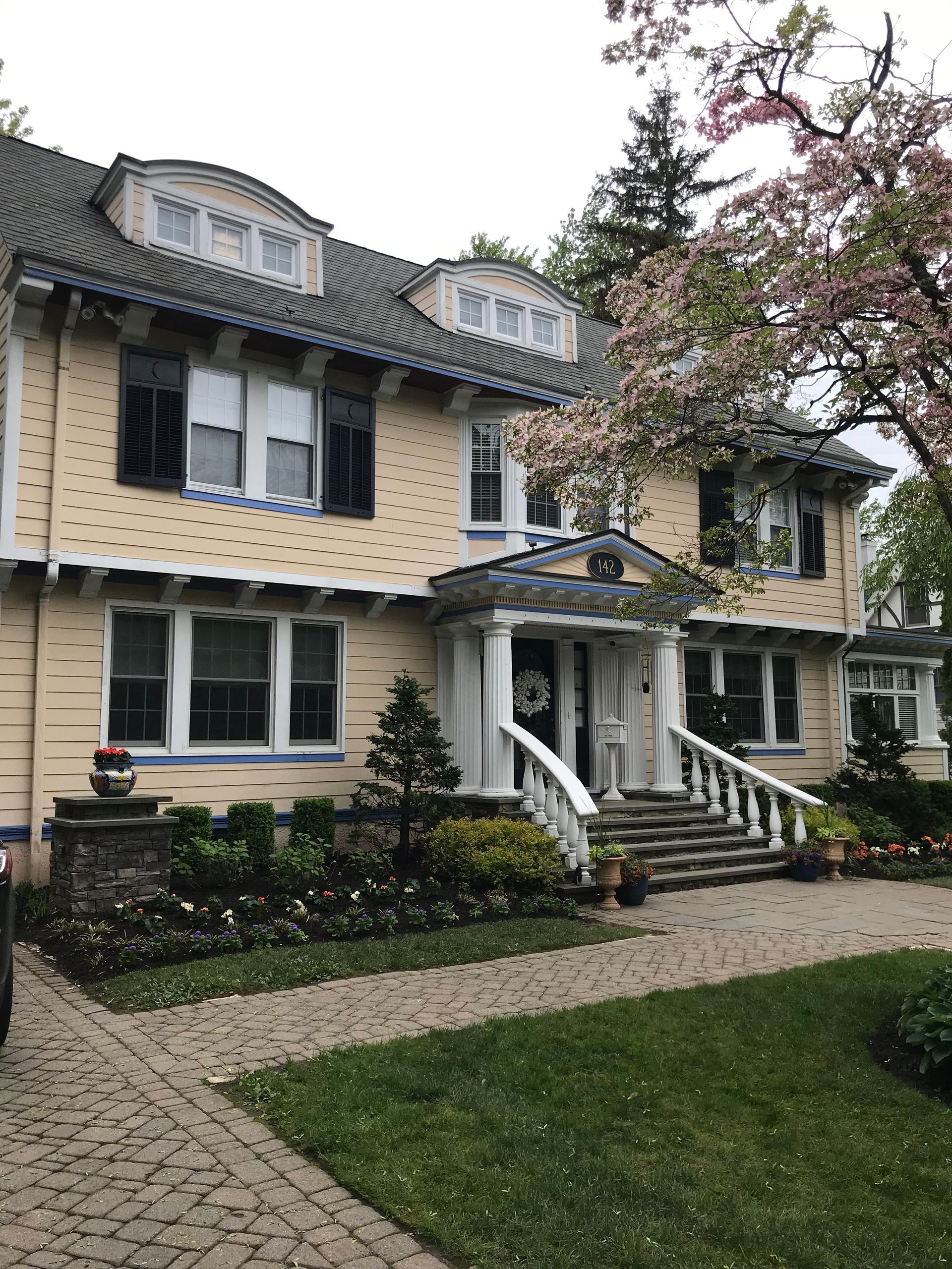 Large cream Victorian house with dark trim, front garden, and stone walkway under blooming trees
