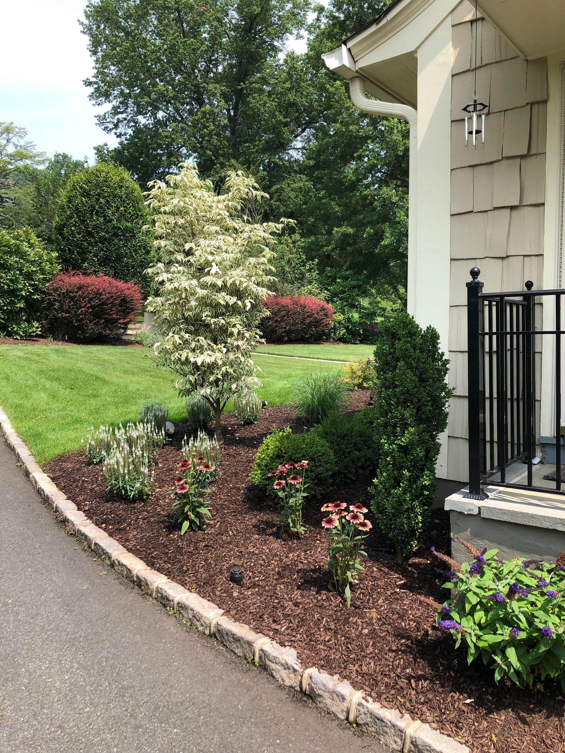 Landscaped front yard with shrubs, mulch, and a stone-edged driveway beside a house porch