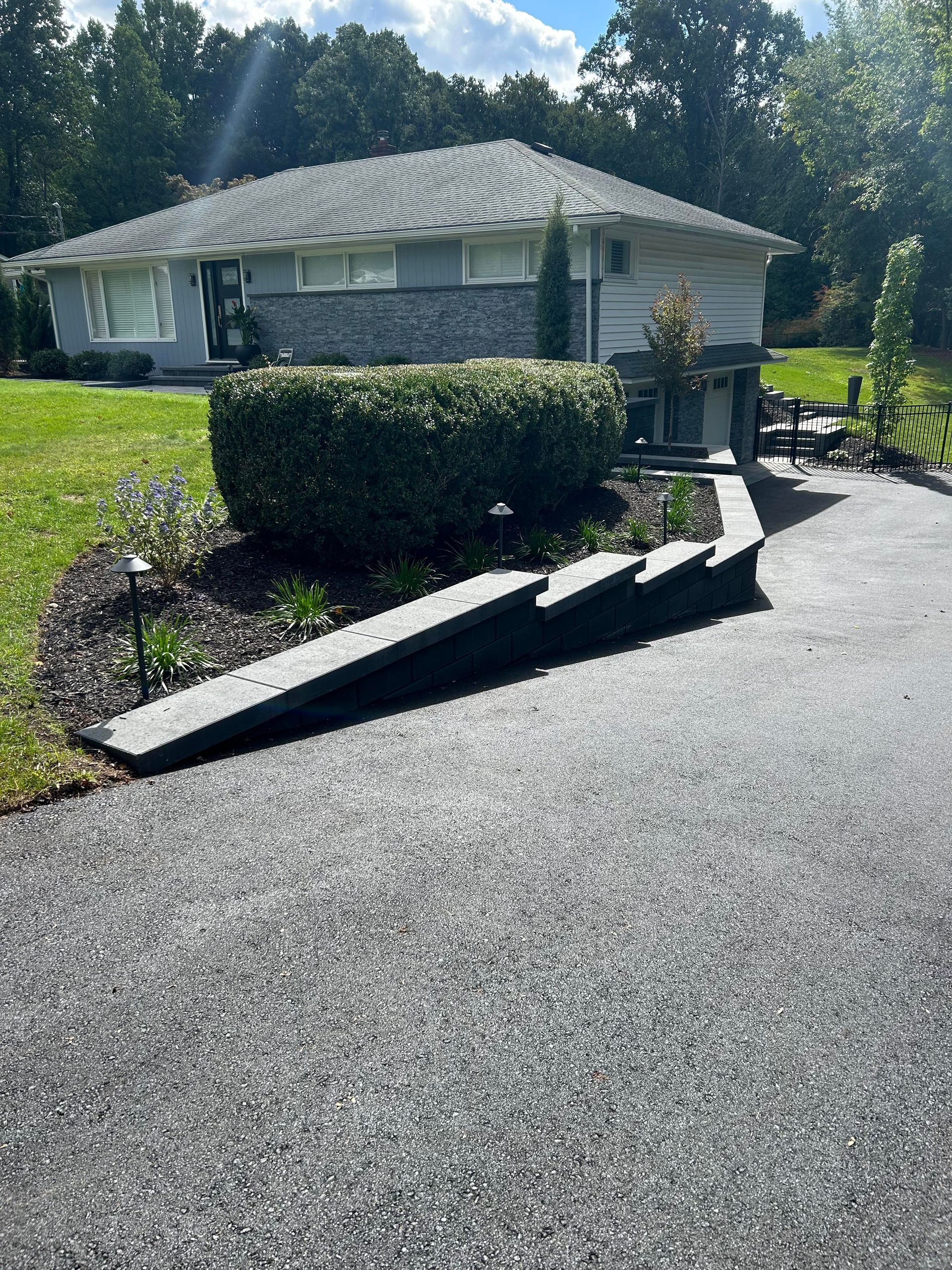 Broken concrete ramp beside a hedge at a house driveway, with a person standing near the entrance.