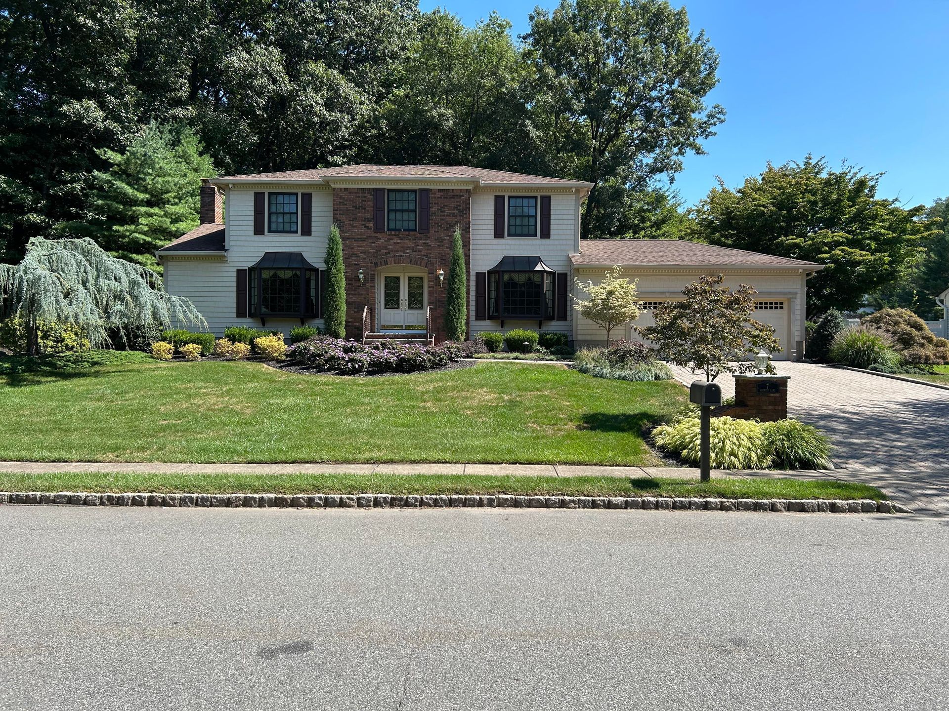 Suburban two-story brick house with a manicured lawn, driveway, and mailbox on a sunny day