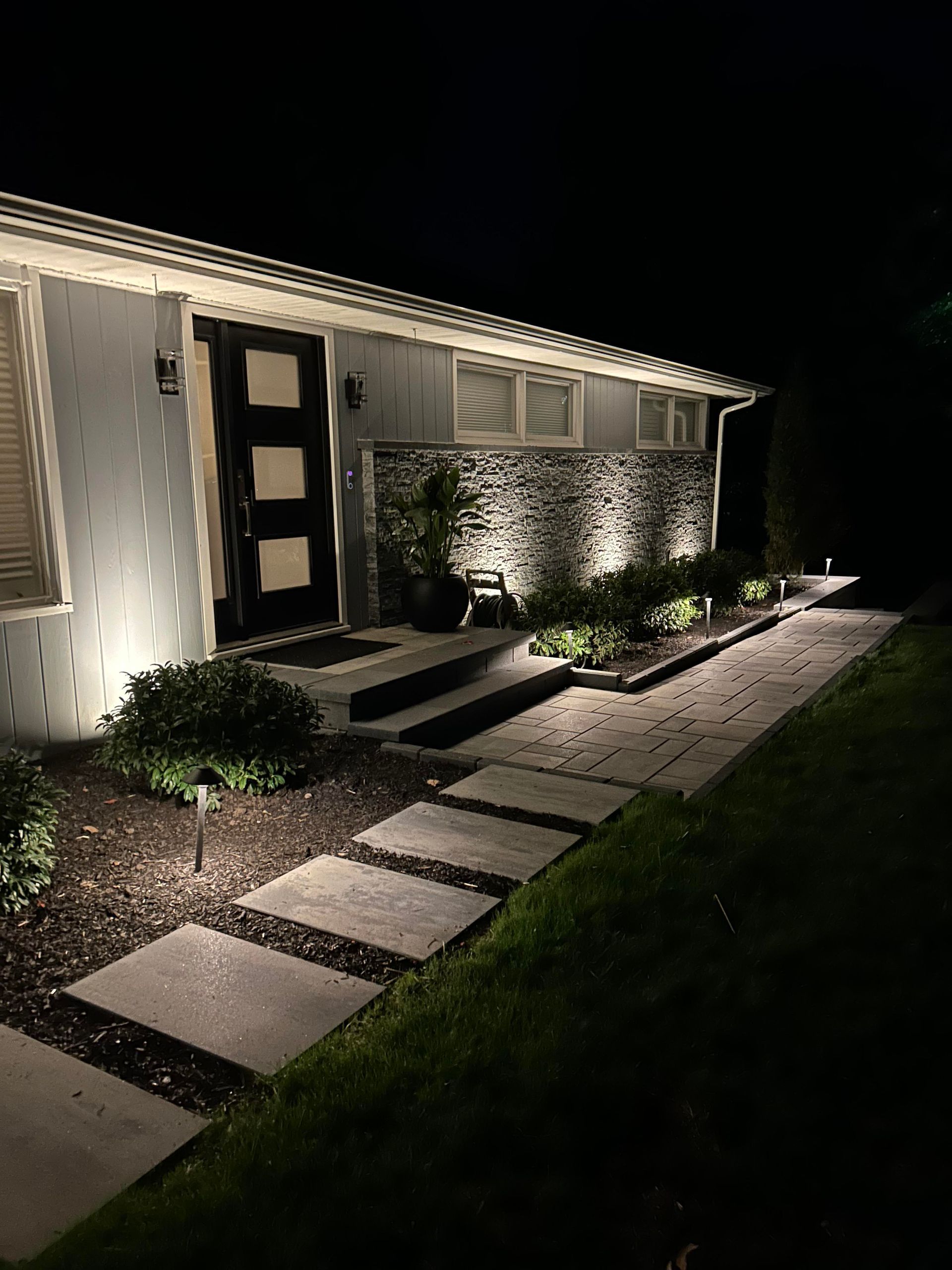 Modern house entry at night with lit walkway, front steps, and landscaped plants