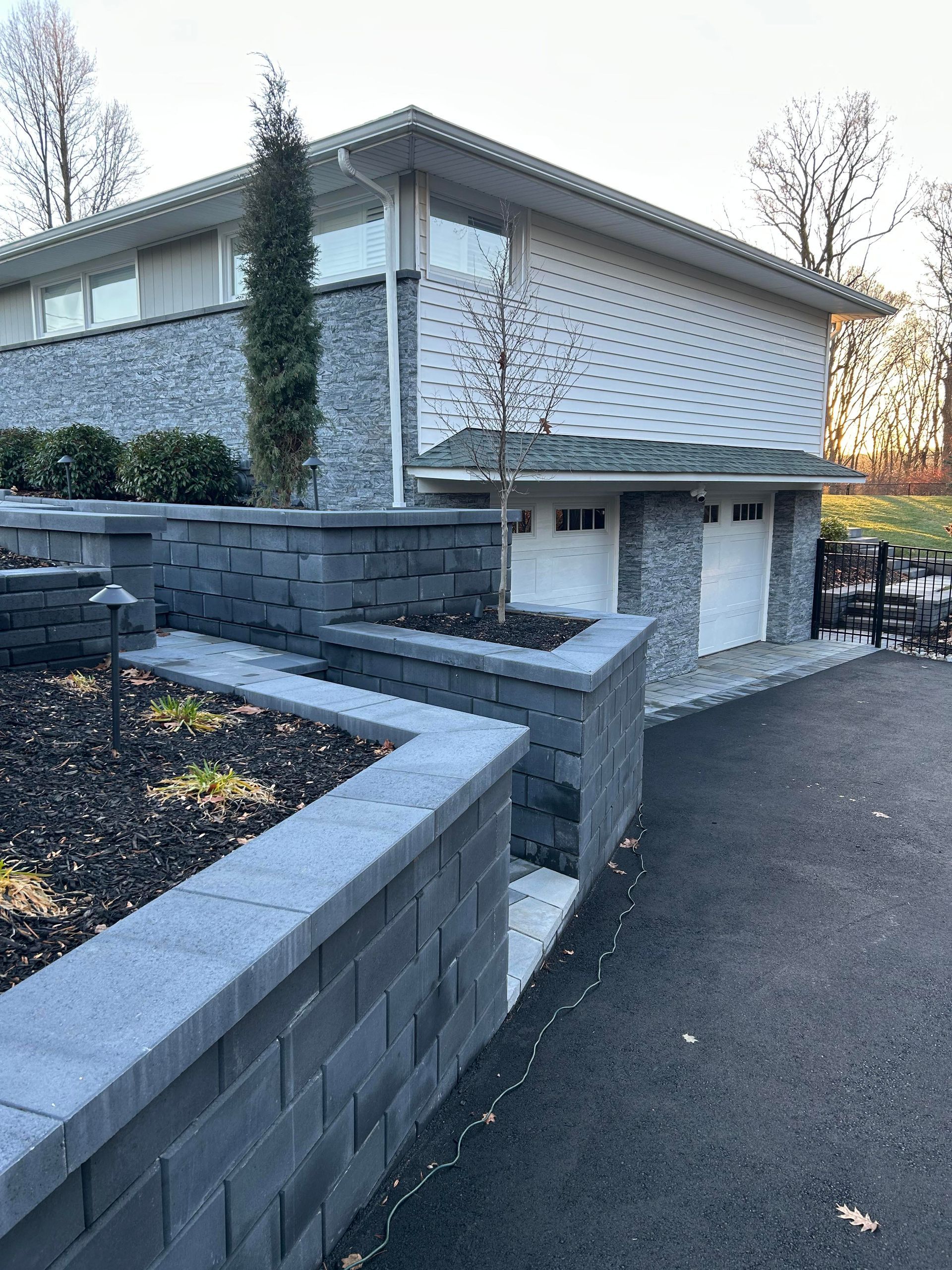 Modern gray stone building with low retaining walls and a paved driveway, viewed from an outdoor corner.