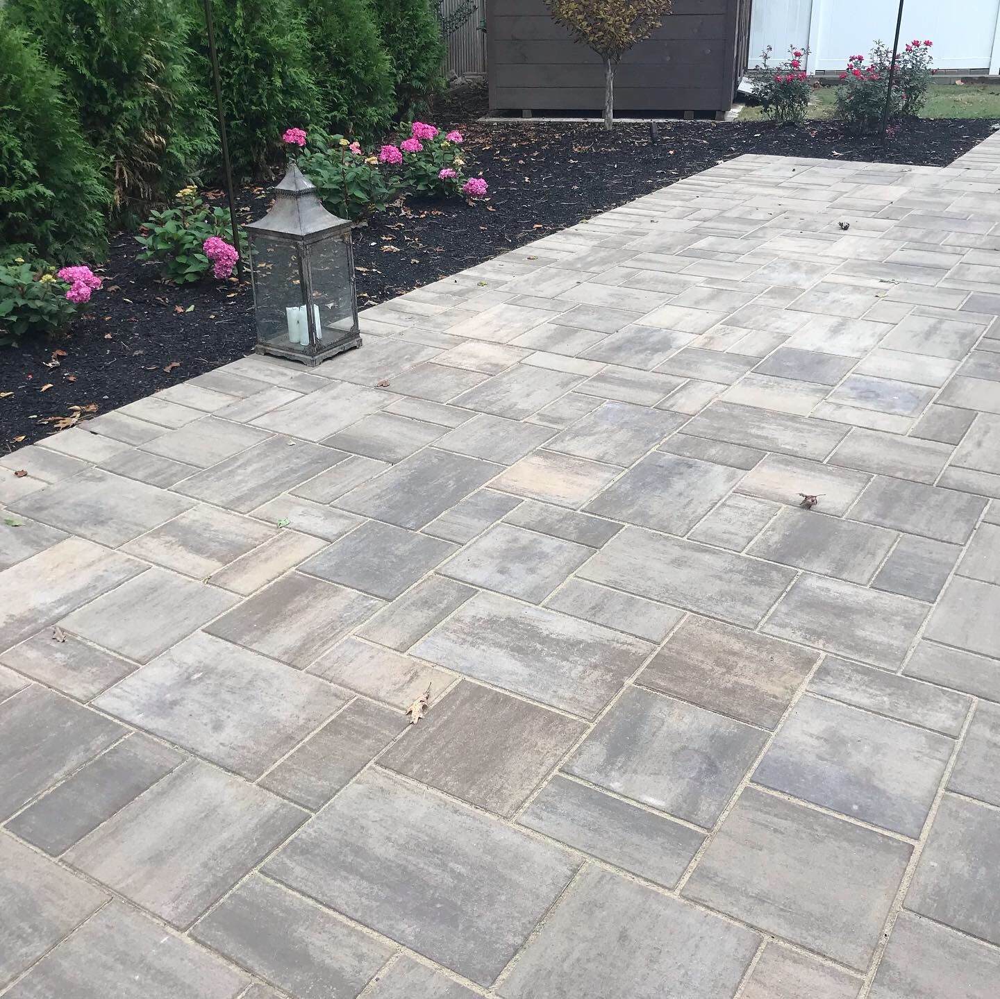 Stone patio walkway beside a garden bed with pink flowers and a lantern