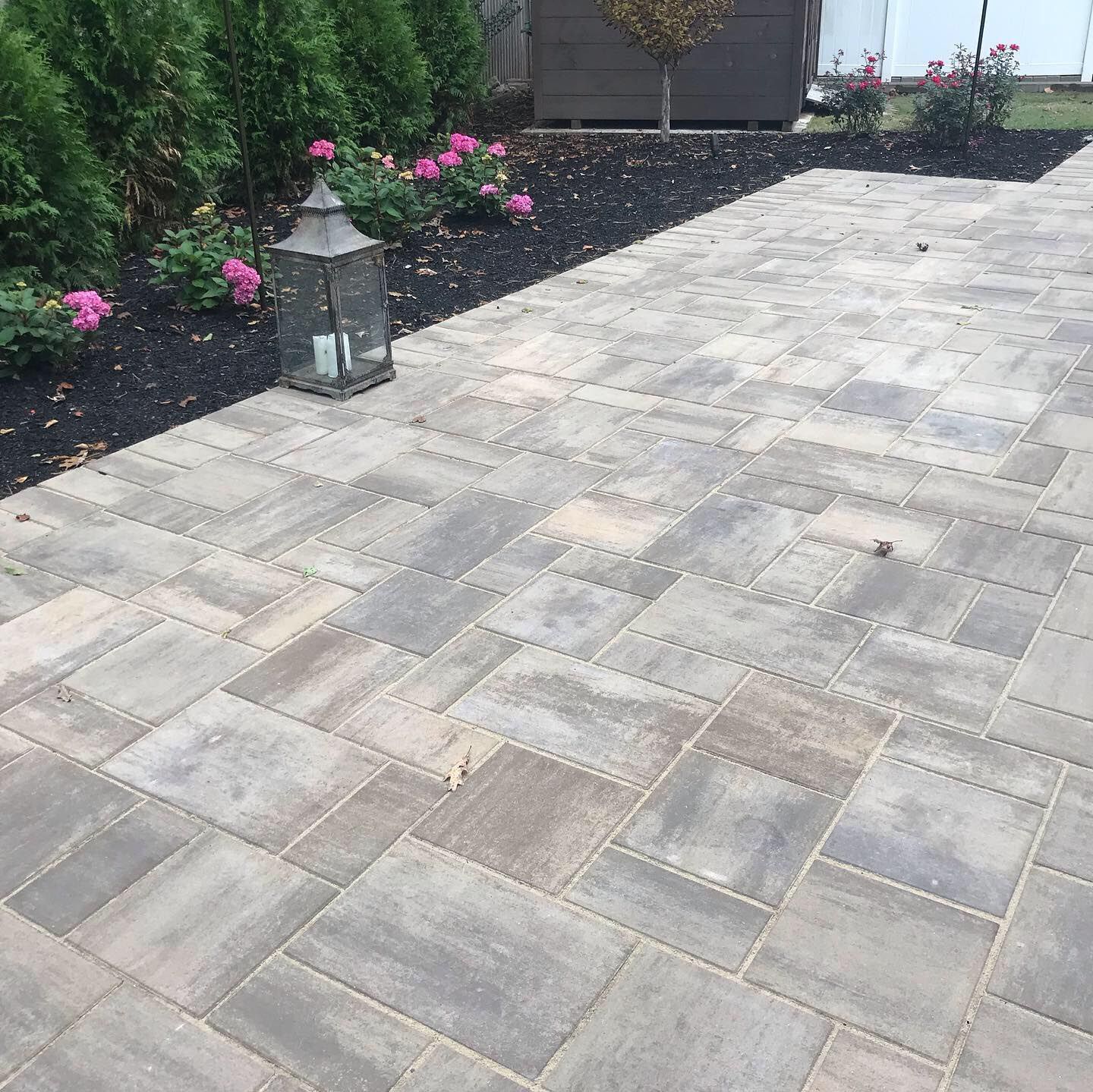 Stone paver patio with a lantern and pink flowers beside a house and garden border