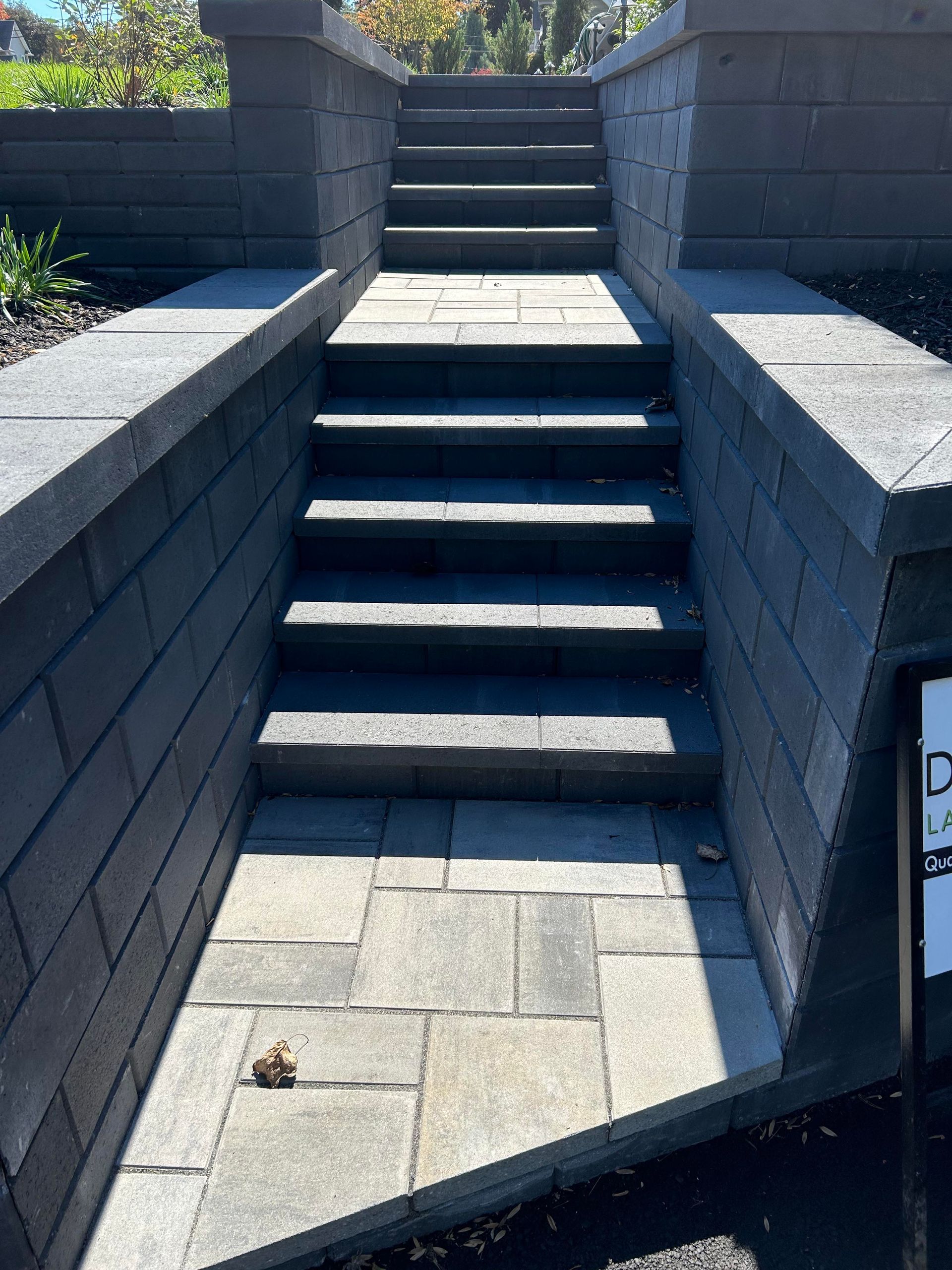 Outdoor stone staircase between retaining walls, with paved landing and bright sunlight.