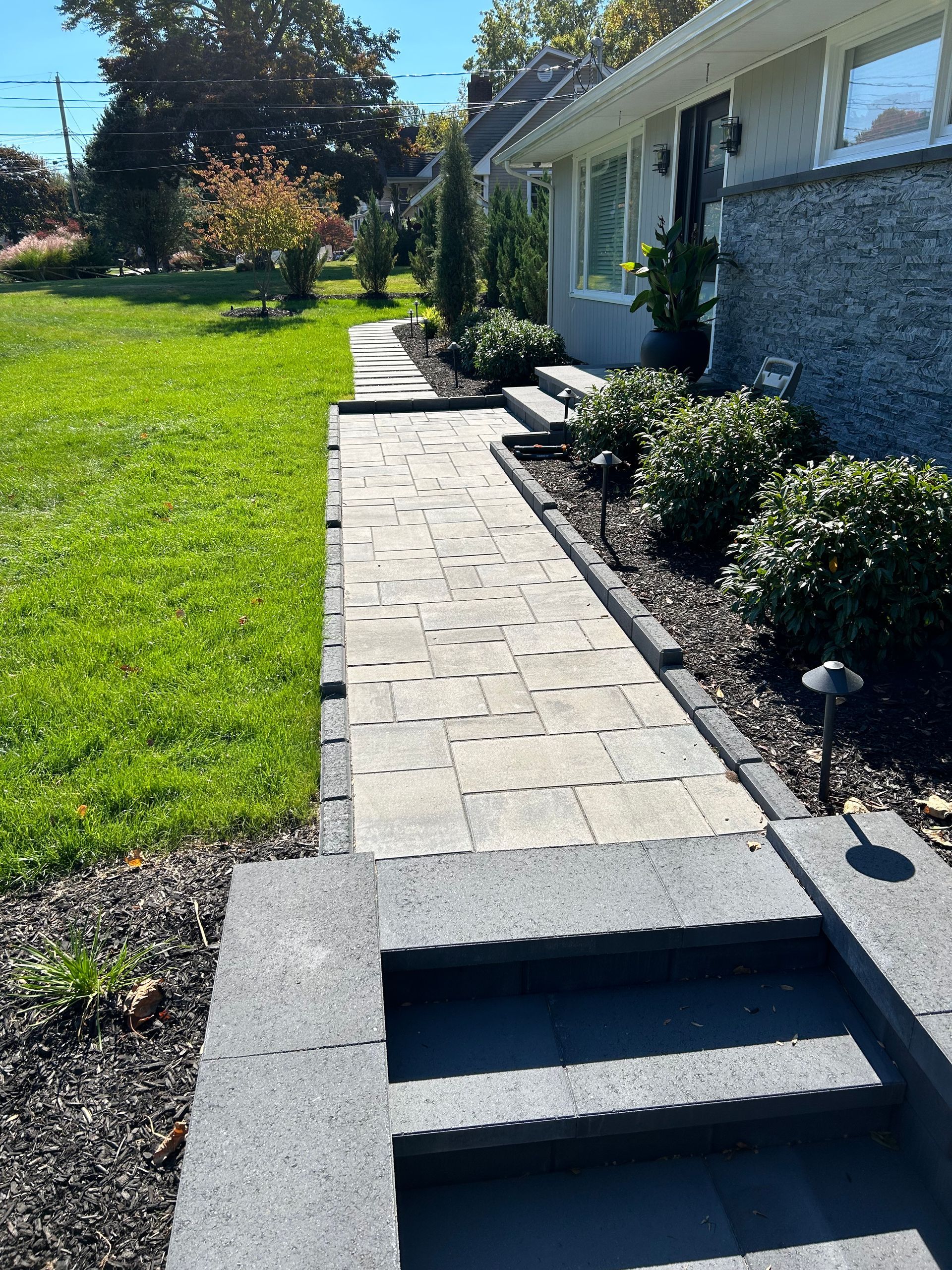 Front walkway with stone steps, a green lawn, and a house exterior in bright sunlight