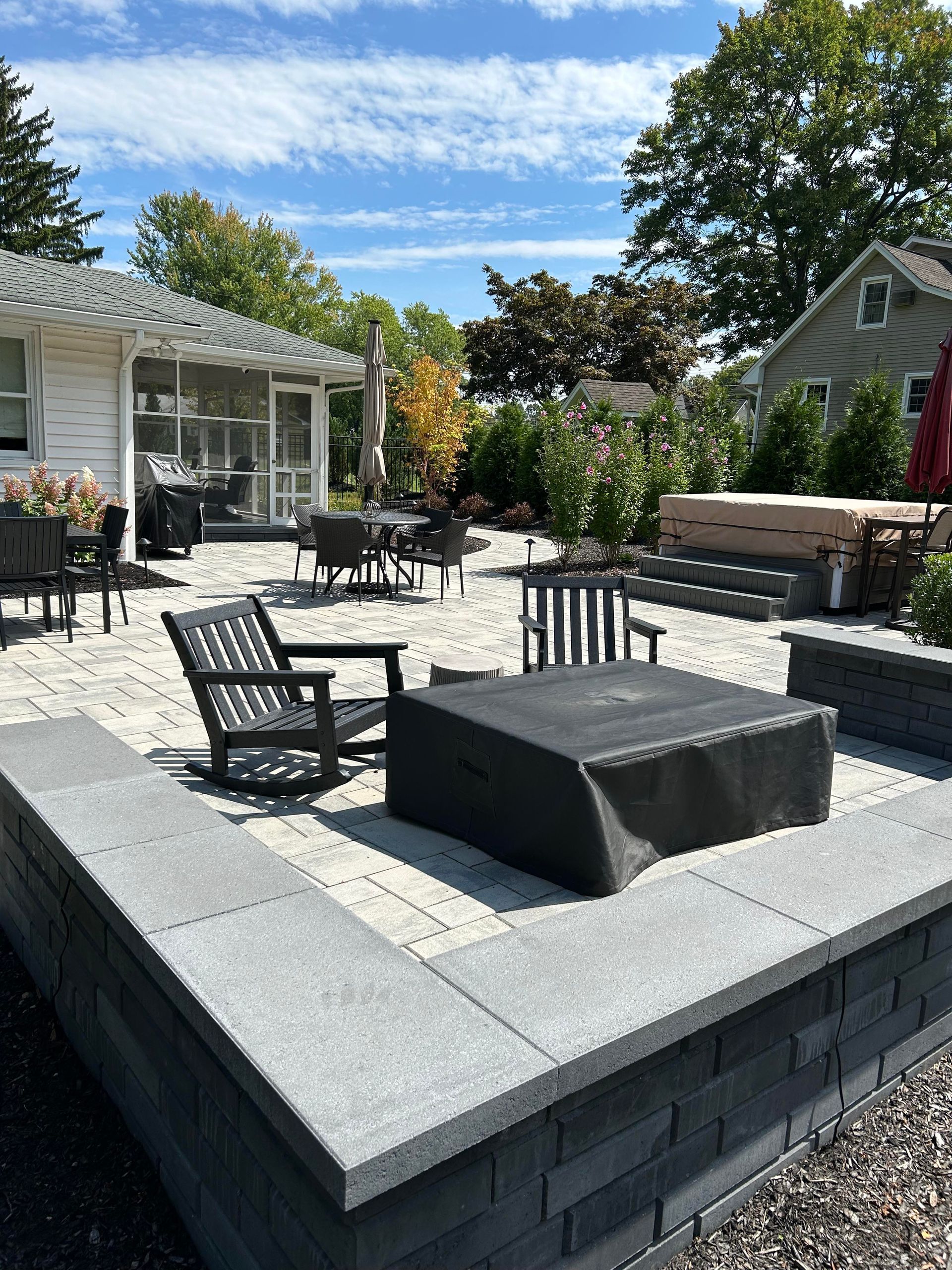 Patio with gray stone seating, black chairs, and a fire pit in a landscaped backyard