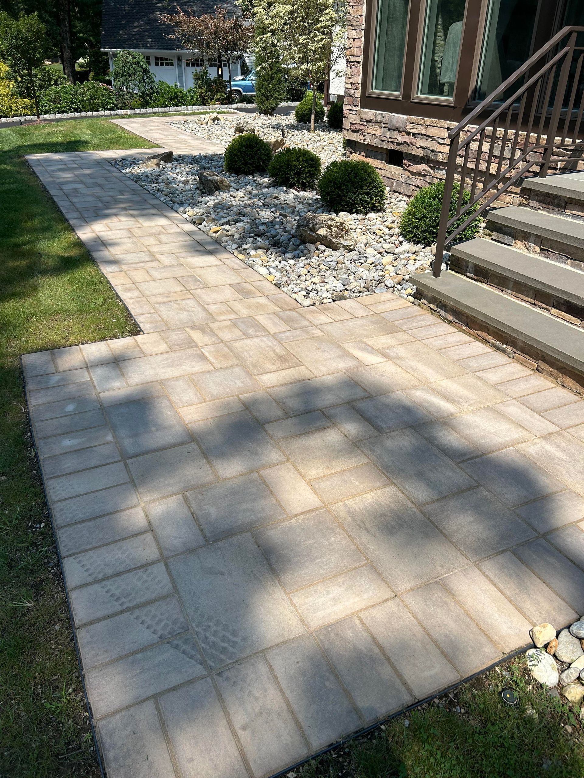 Paver walkway beside stone steps and landscaped shrubs in a sunny front yard