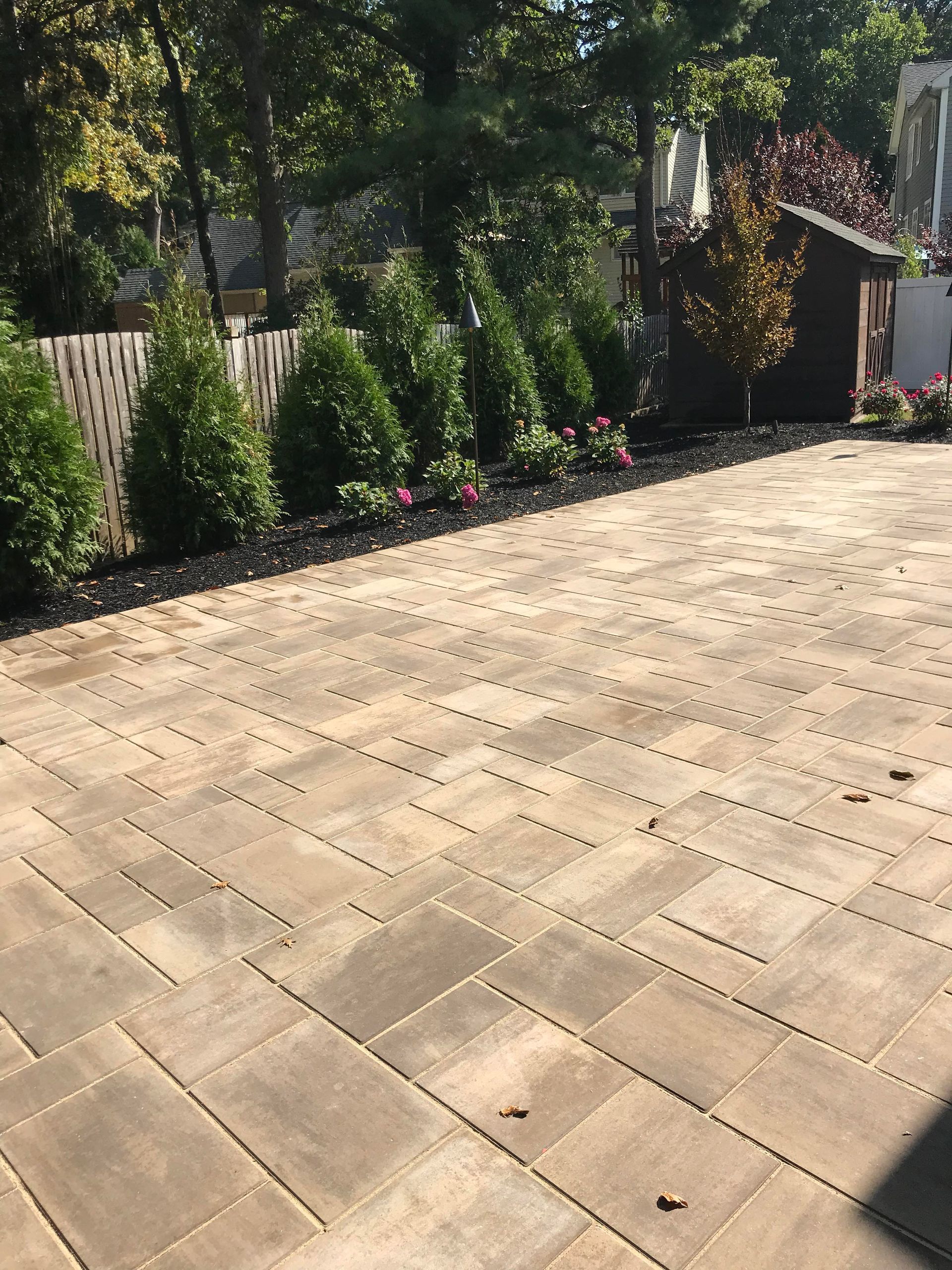 Sunlit brick patio beside a hedge-lined garden and small wooden shed