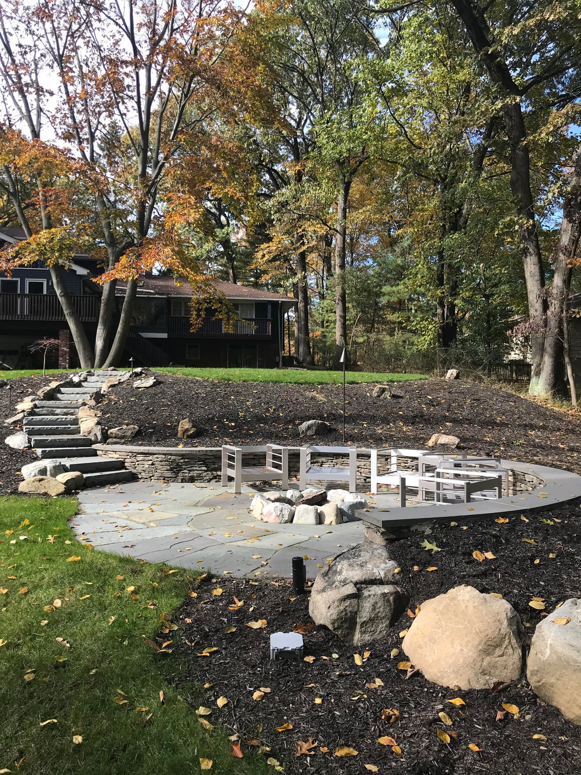 Stepped stone patio with circular fire pit area and autumn trees in a backyard