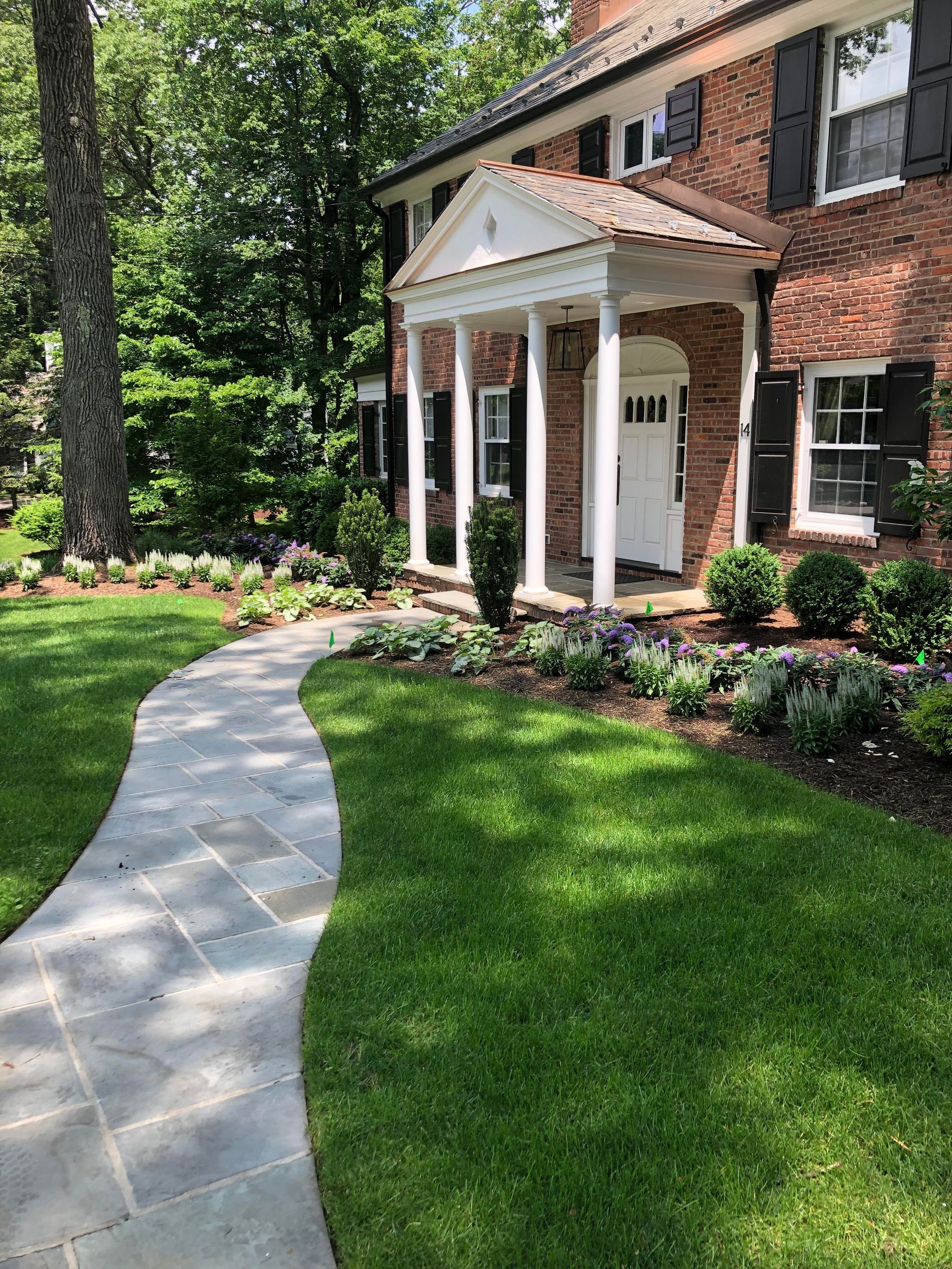 Brick house entrance with white columns, curved walkway, and landscaped green lawn.