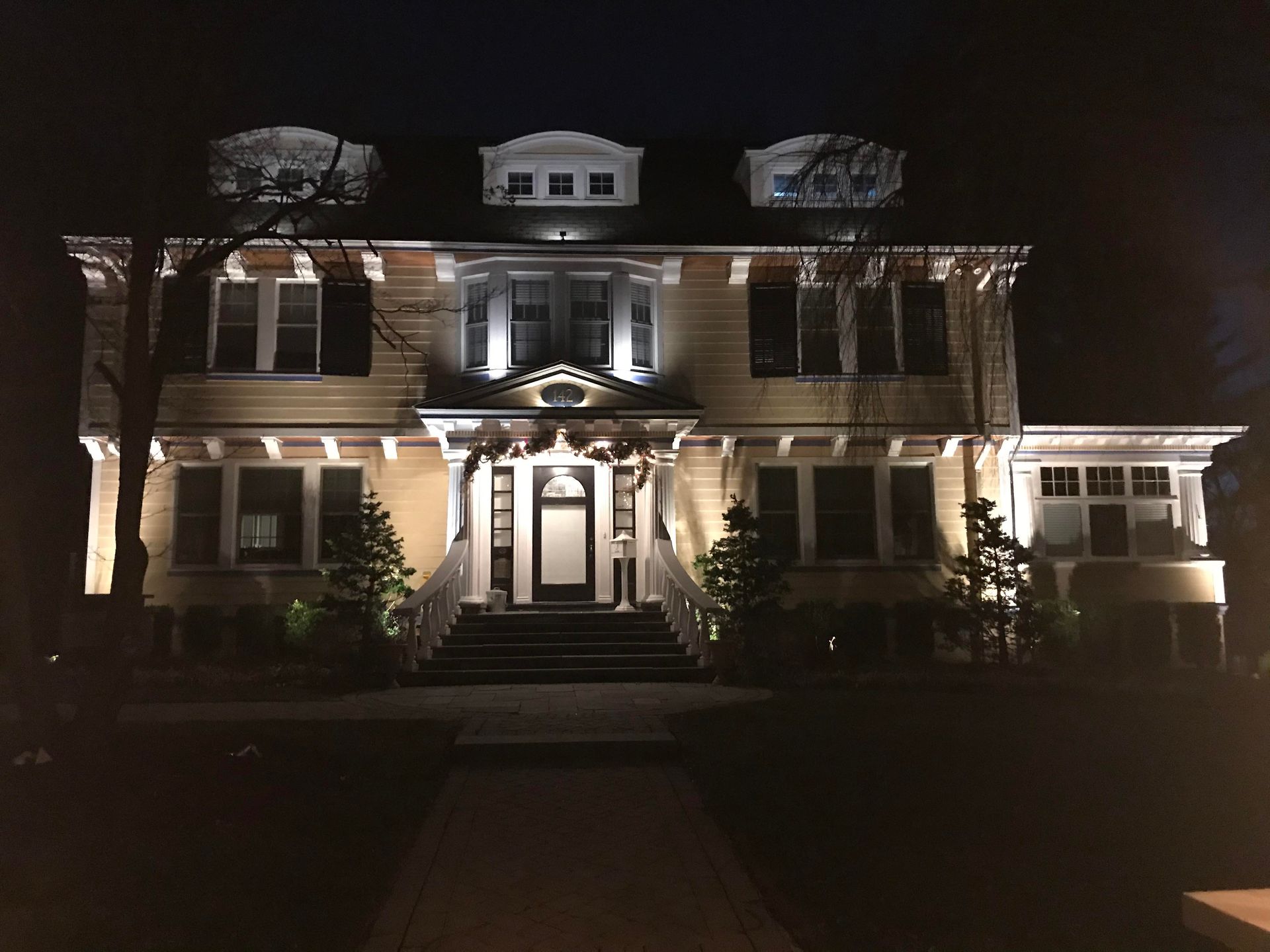 Illuminated brick house at night with symmetrical porch and dormer windows