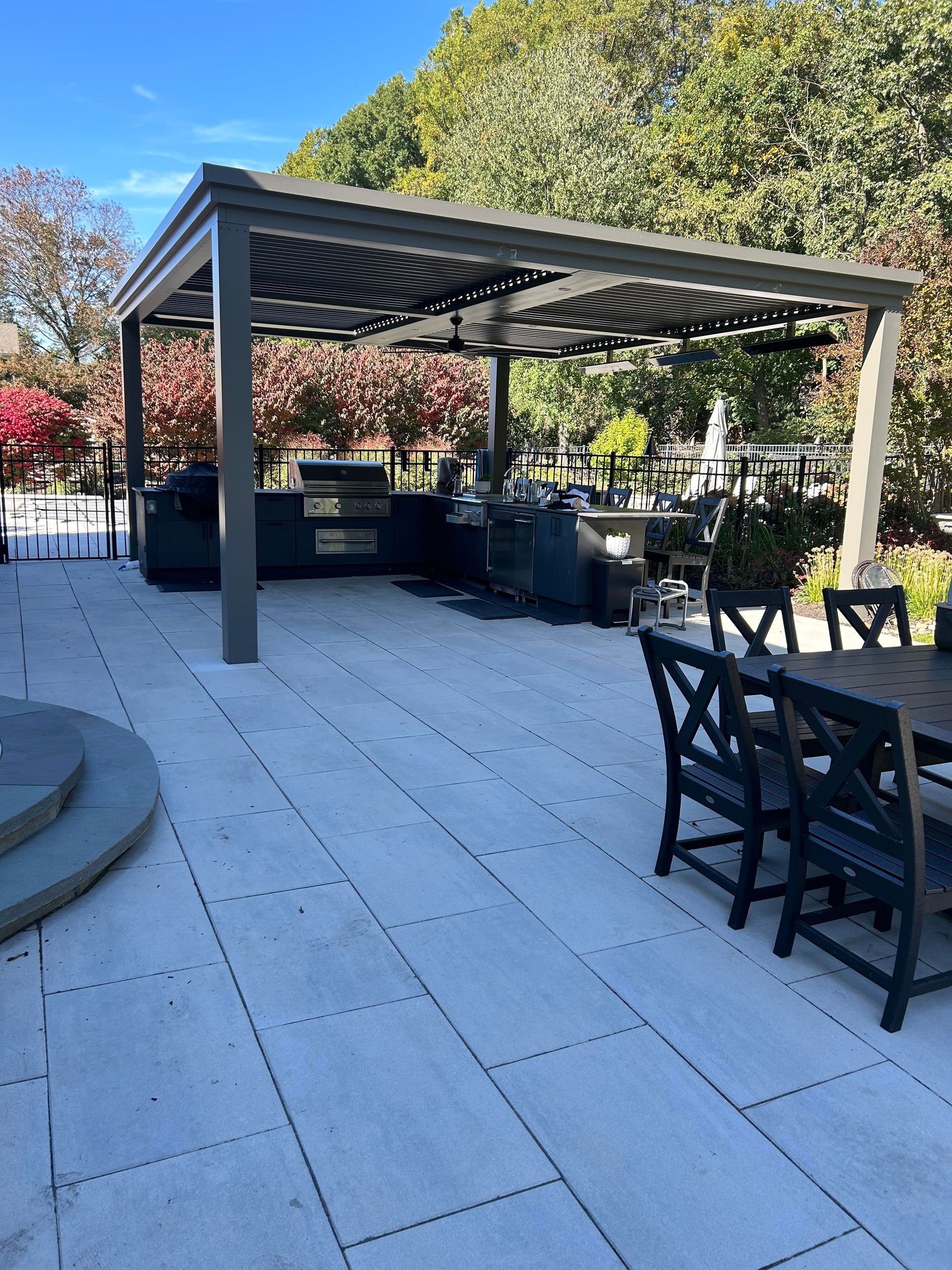 Outdoor patio with pergola, tables, and chairs on stone paving, surrounded by trees and greenery