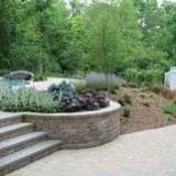 Stone planter with dark purple flowers beside steps in a landscaped garden