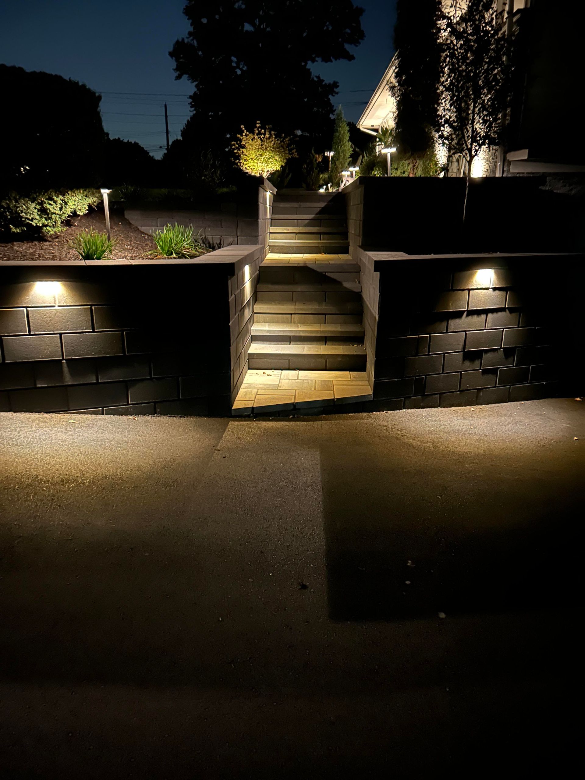 Lit stone steps in a landscaped garden at night, flanked by low walls and pathway lights