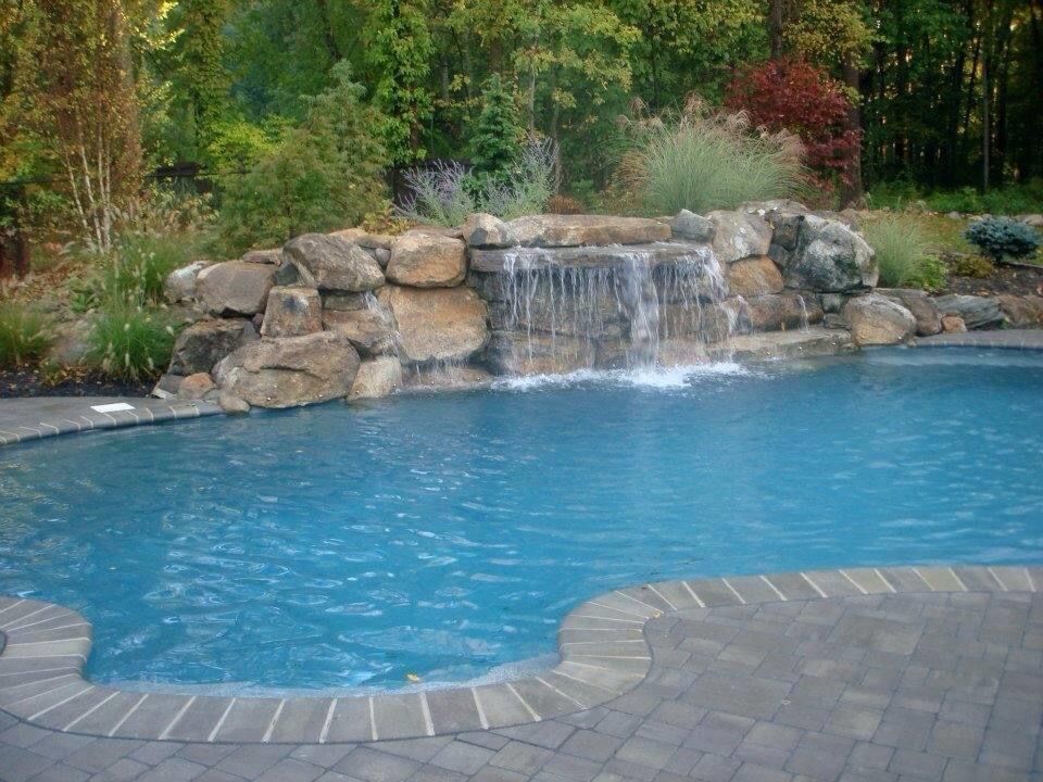 Backyard pool with a rock waterfall and lush greenery surrounding the blue water