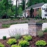 Landscaped front yard with stone pillars, flowers, and a house in the background