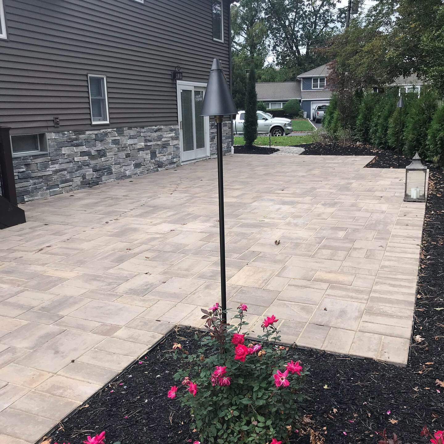 Backyard patio with stone pavers, a flower bed, and a tall umbrella stand