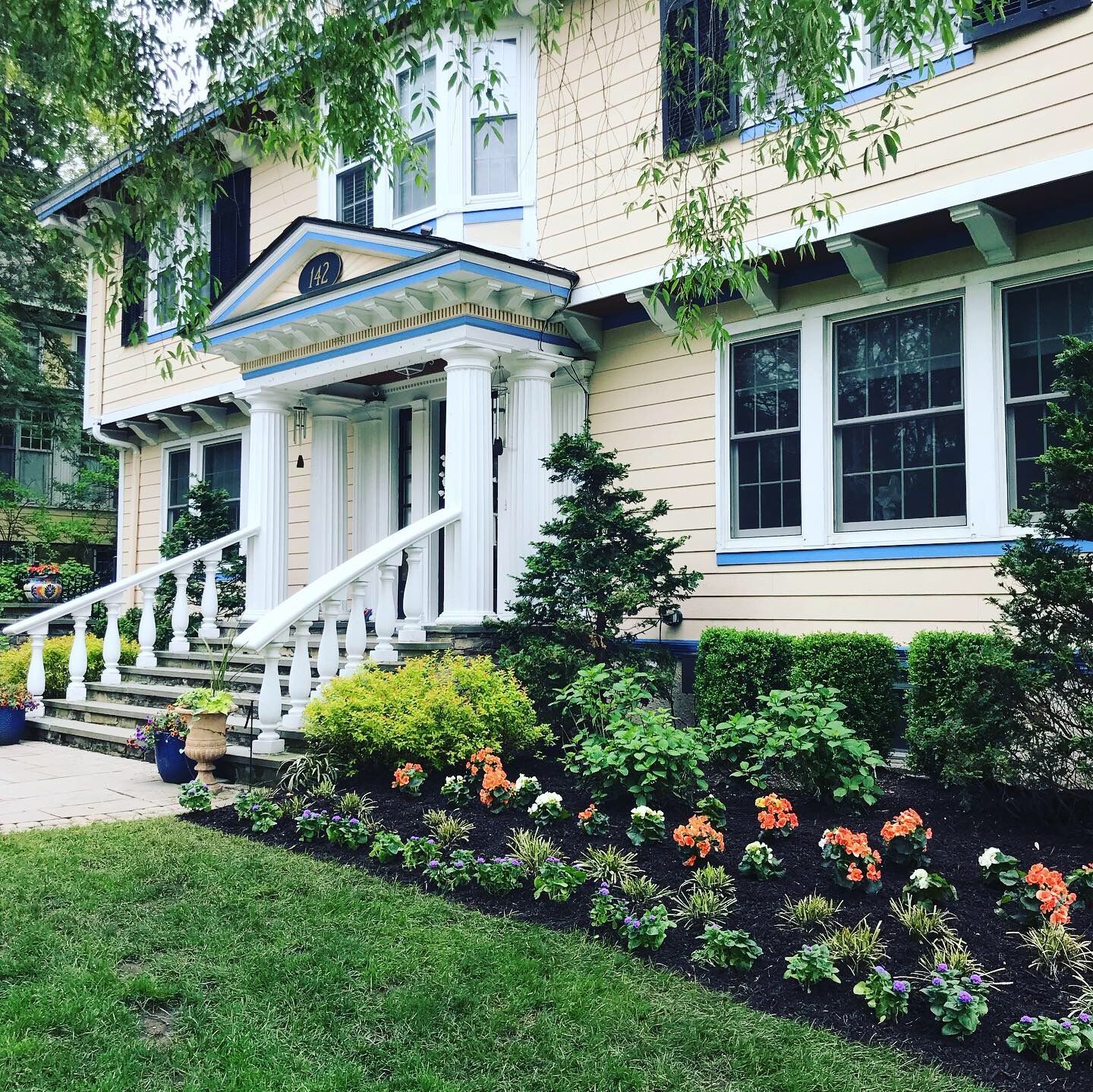 Cream house with white columns, front porch, and landscaped garden in the foreground