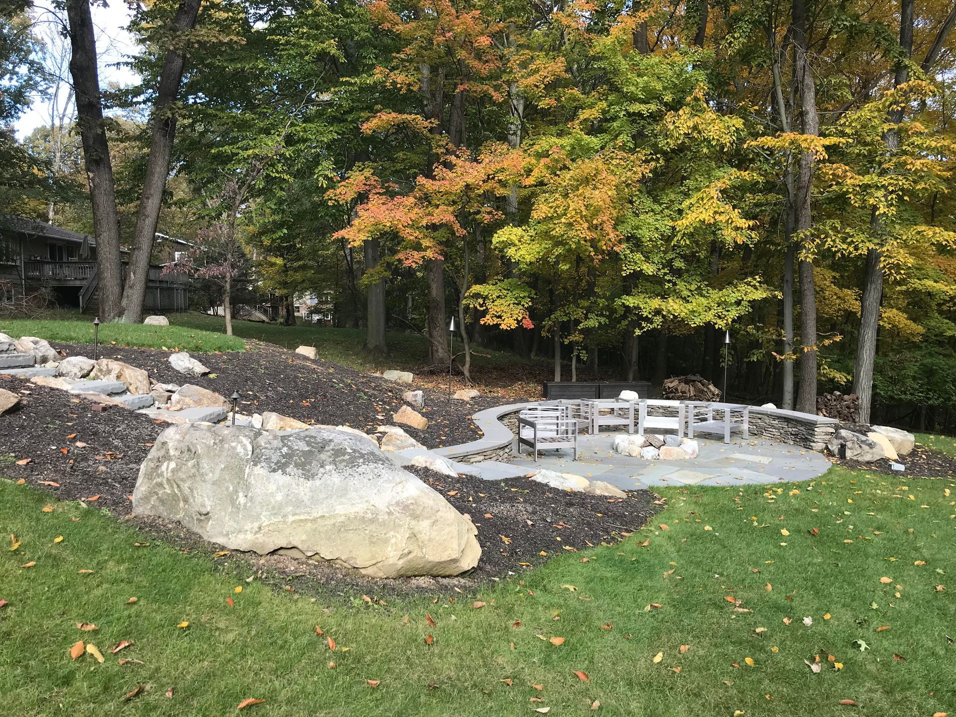 Backyard fire pit area with stone seating, large boulders, and autumn trees