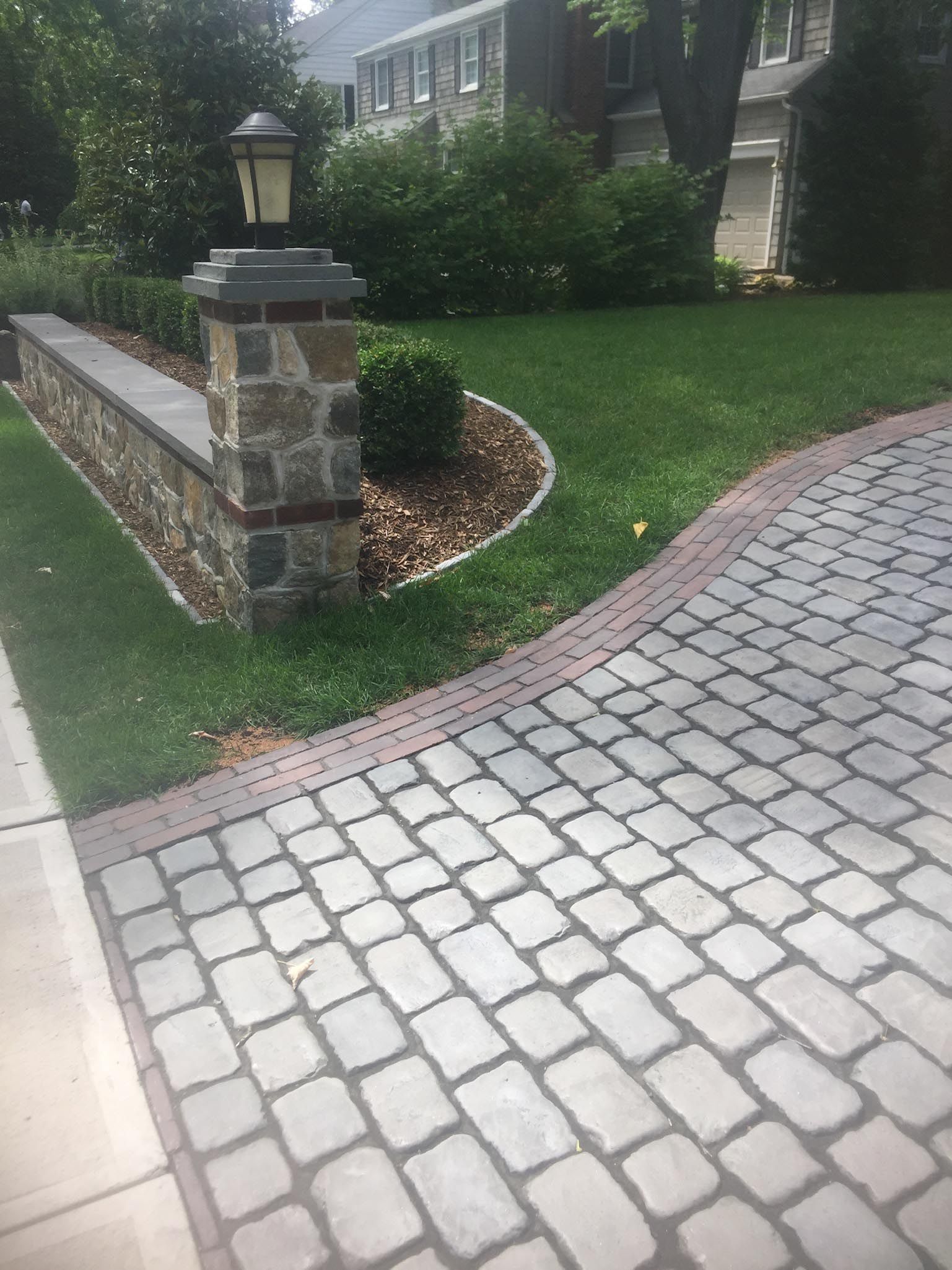 Stone-paver driveway beside a low stone wall and green lawn in front of a house