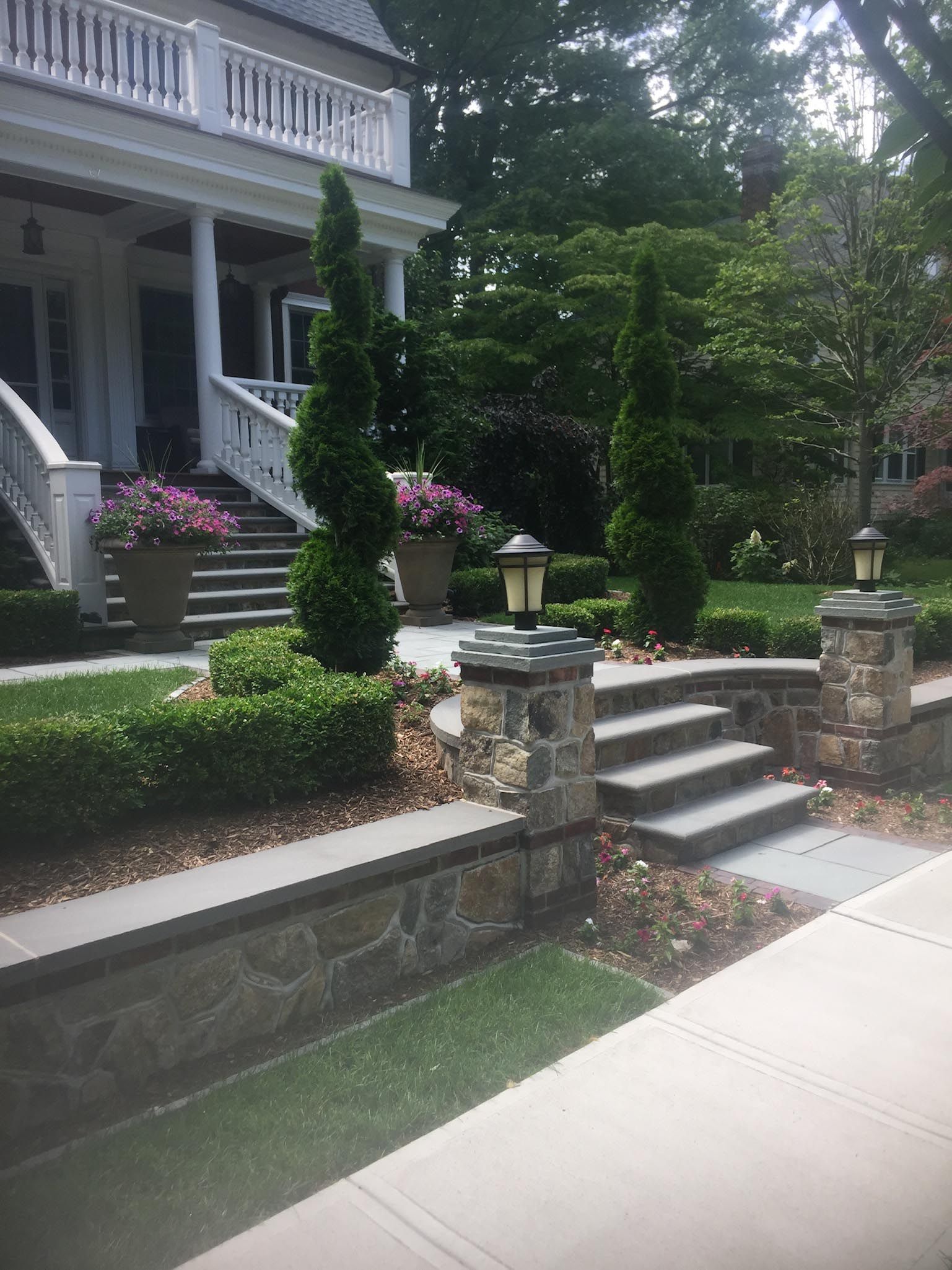 House entrance with stone steps, manicured shrubs, and flower baskets along a sidewalk