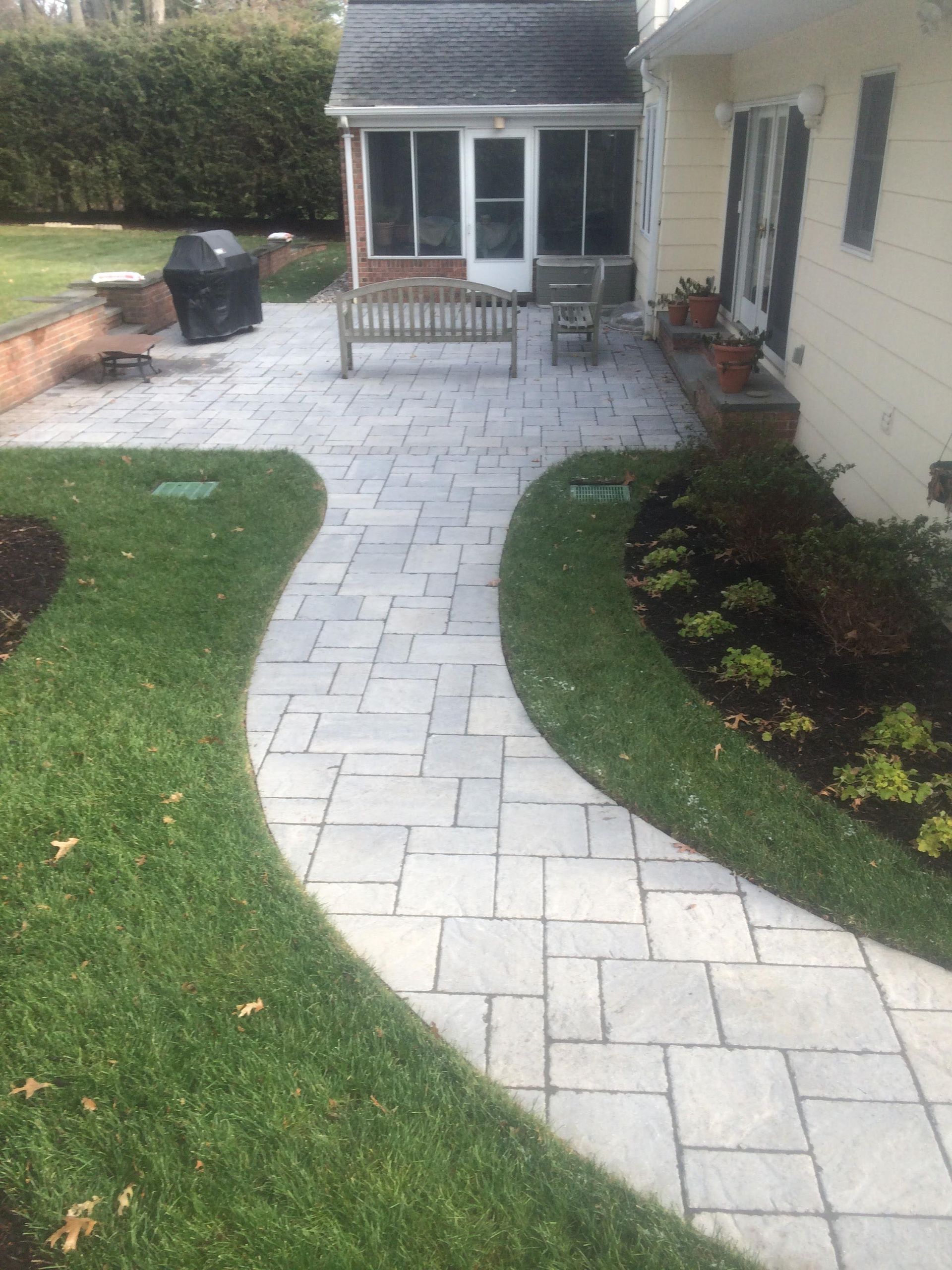 Curved stone walkway through a lawn to a house patio with black bench and potted plant