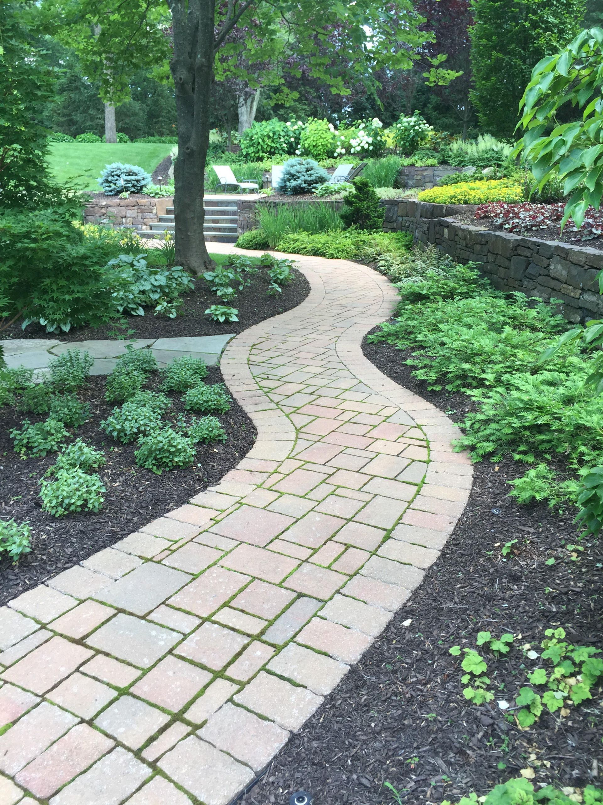 Curved brick garden path winding through lush green landscaping and trees