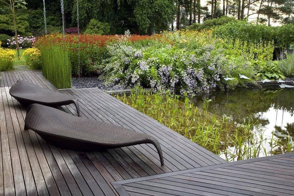 Modern lounge chair on a wooden deck beside a pond in a landscaped garden