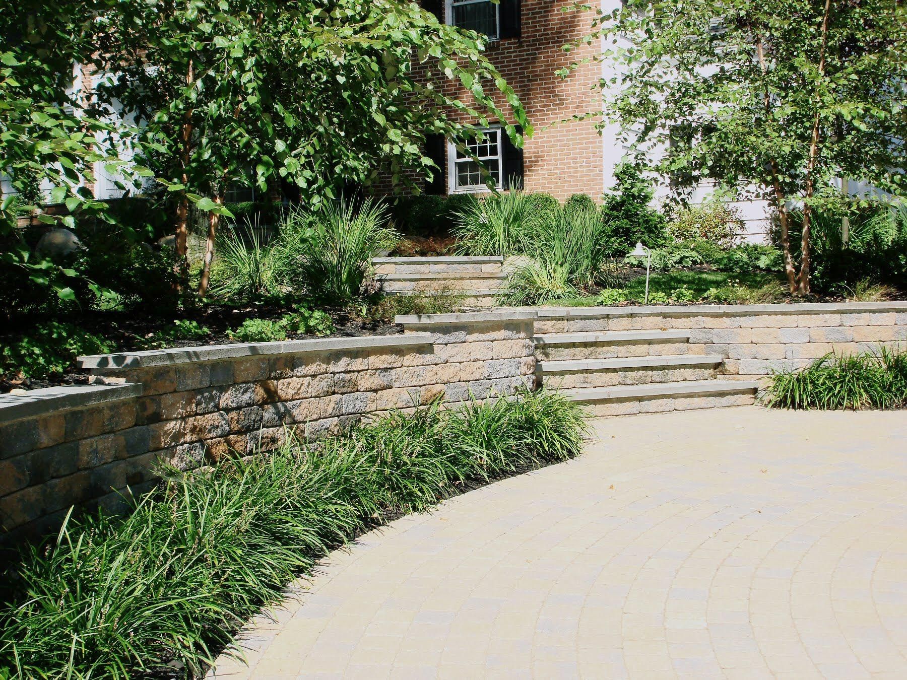 Curved stone patio and steps leading to a brick house, surrounded by lush green landscaping