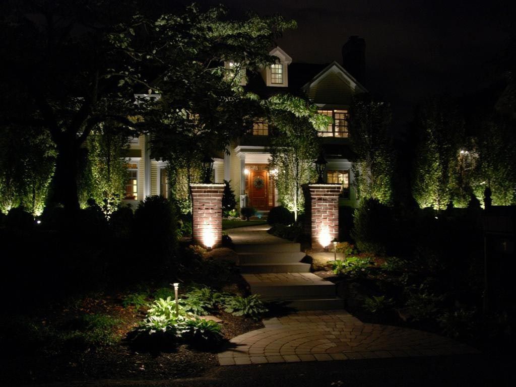 Dimly lit house entrance with brick path, glowing garden lights, and trees at night