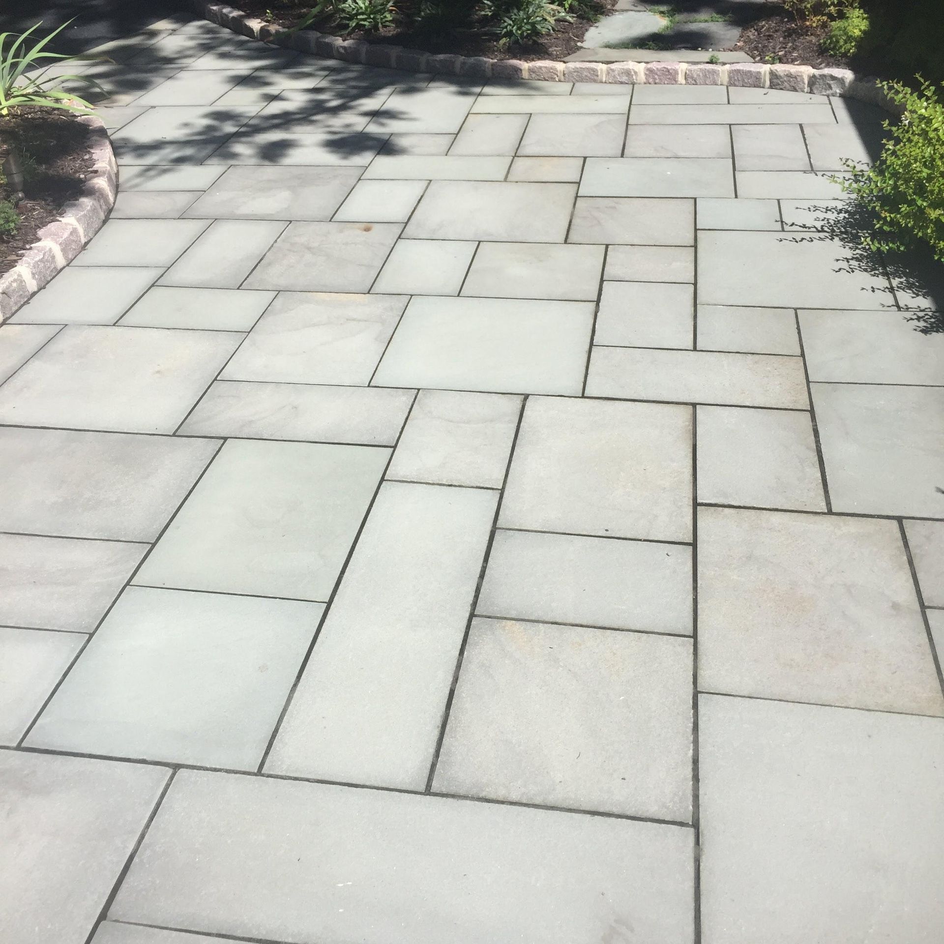 Stone walkway with light gray pavers and bordering plants in a sunlit garden
