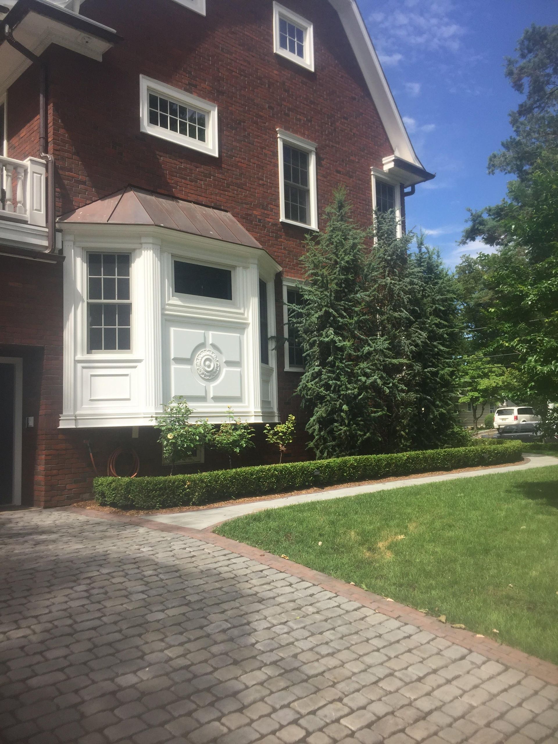 Brick house with white bay window and green lawn beside a cobblestone driveway