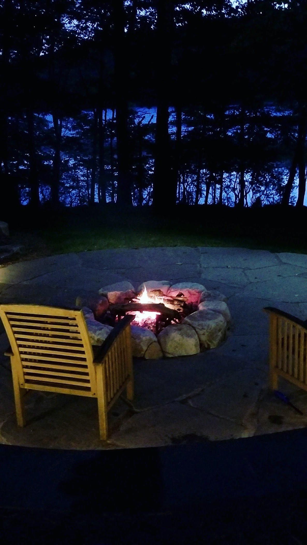 Fire pit glowing in a dark wooded patio, flanked by two wooden chairs.